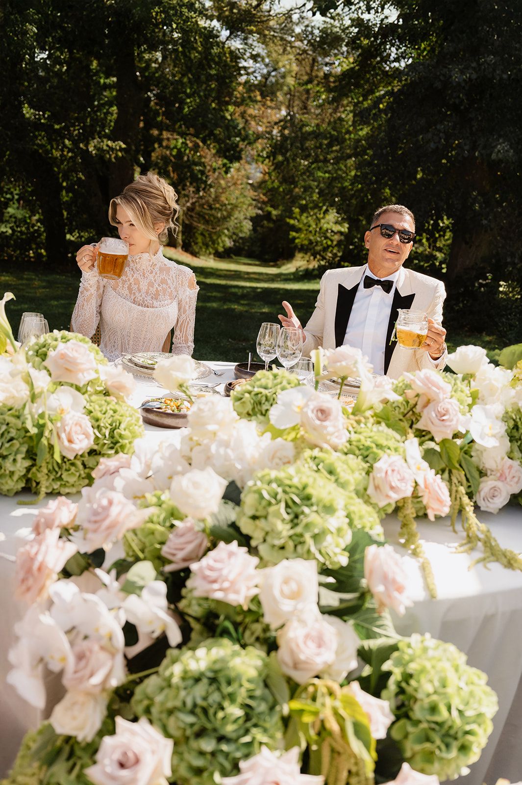Luxurious wedding table decorated with pink roses and green hydrangeas in natural sunlight.