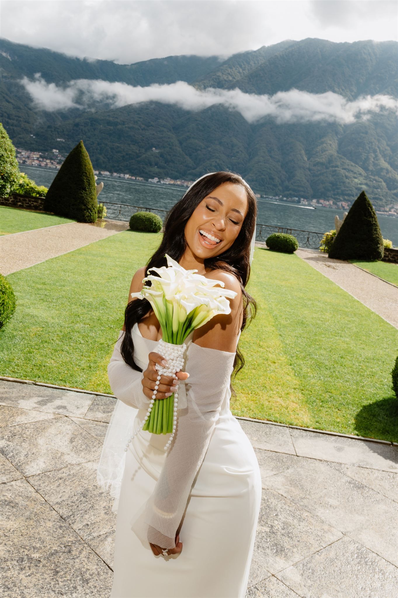 Bride in white dress holds a calla lily bouquet against mountainous landscape backdrop.