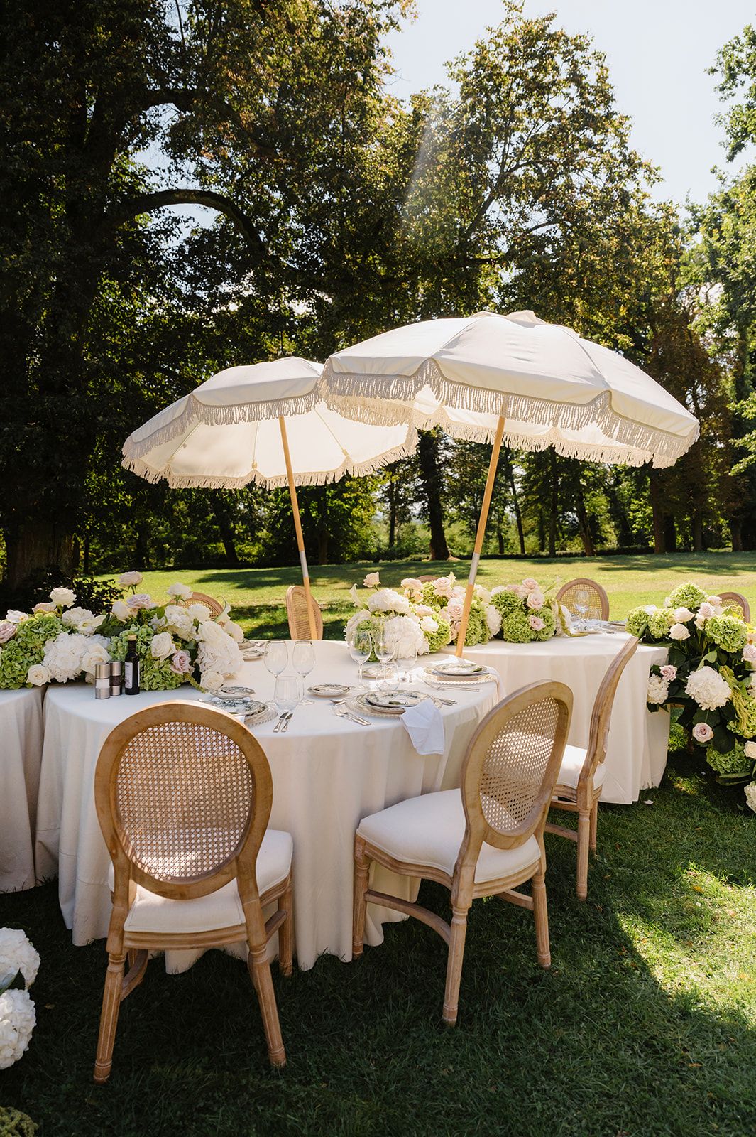 Elegant outdoor wedding reception setup with white parasols and rattan chairs on a lush green lawn.