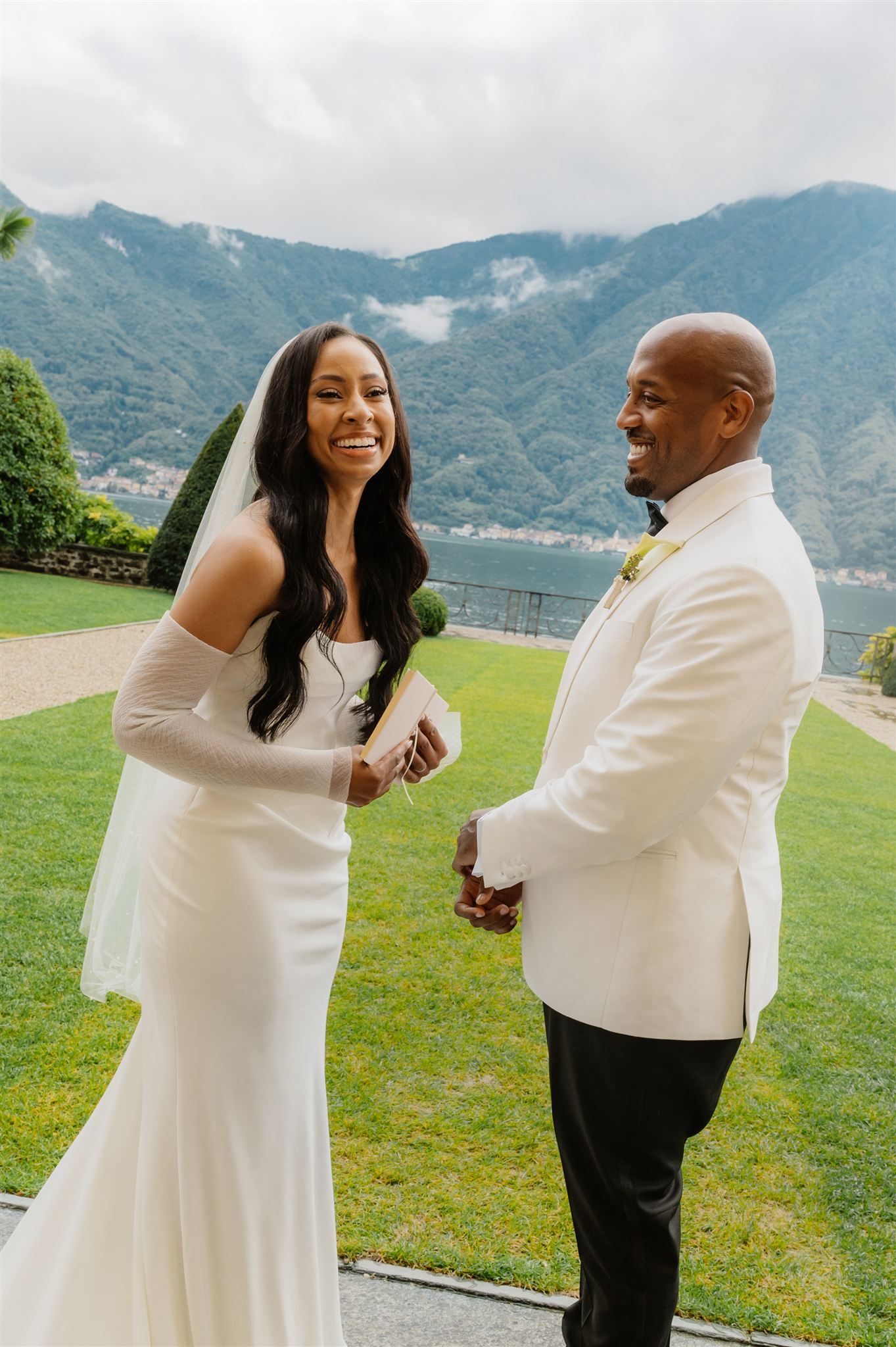 A joyful wedding couple shares laughter during their first look moment in a garden setting.