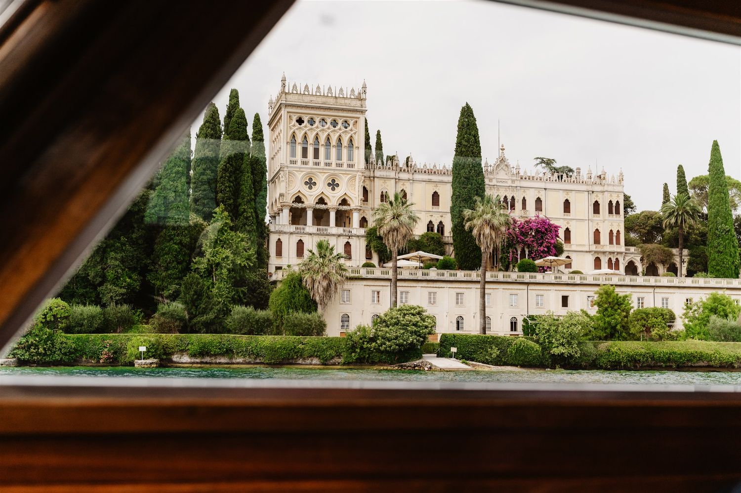 Panoramic view of an elegant Italian villa with cypress trees along Lake Garda's shoreline.