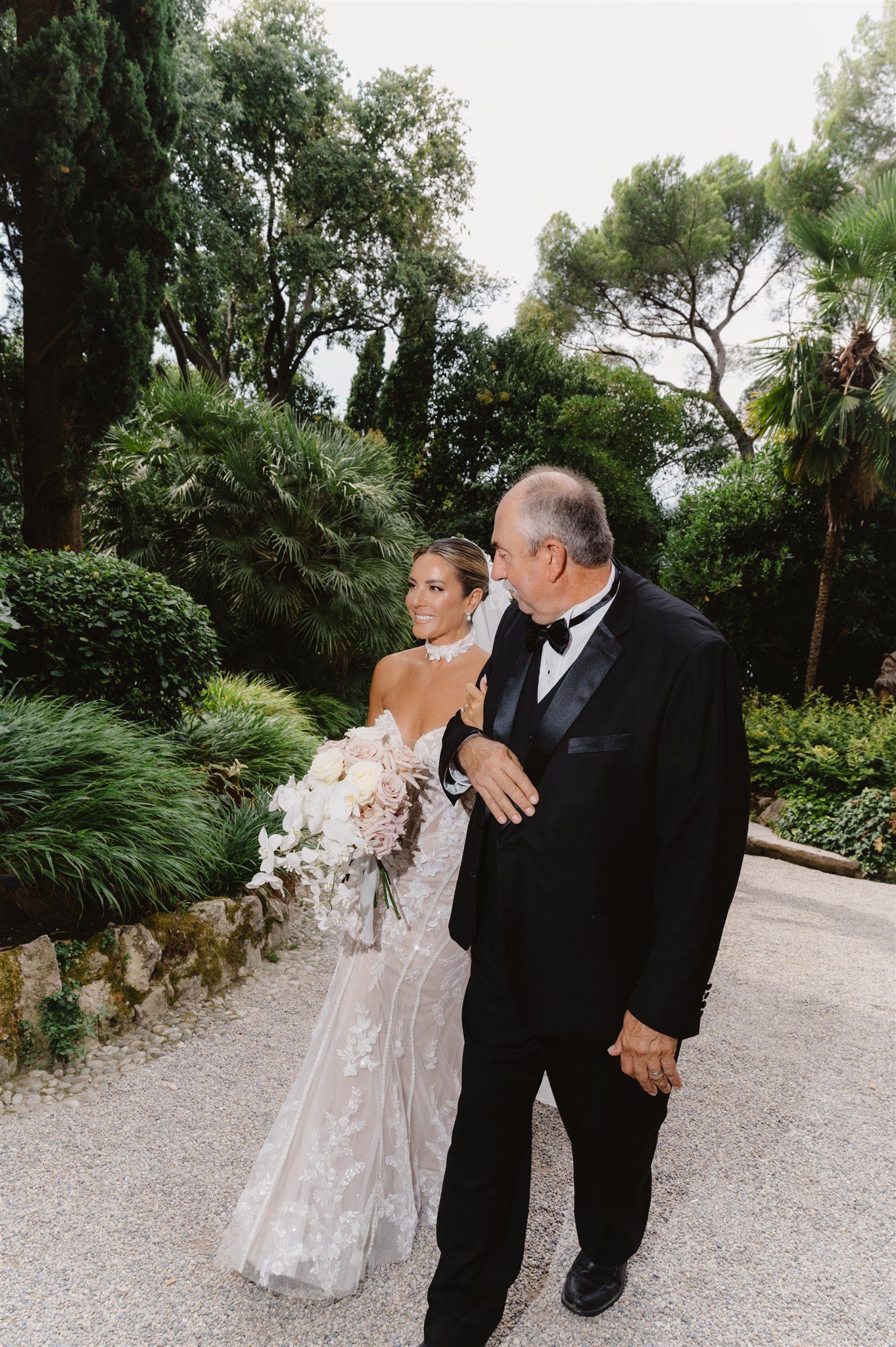 Outdoor wedding photography on gravel path surrounded by lush greenery.