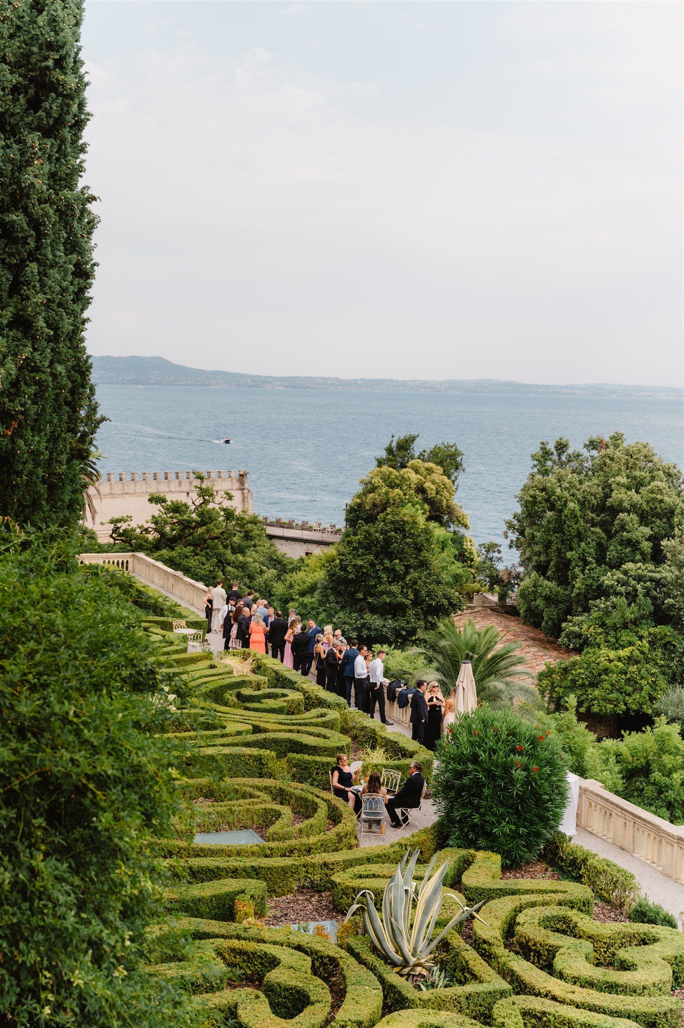Formal garden with manicured hedges and geometric patterns overlooking a scenic coastline. Isola del Garda