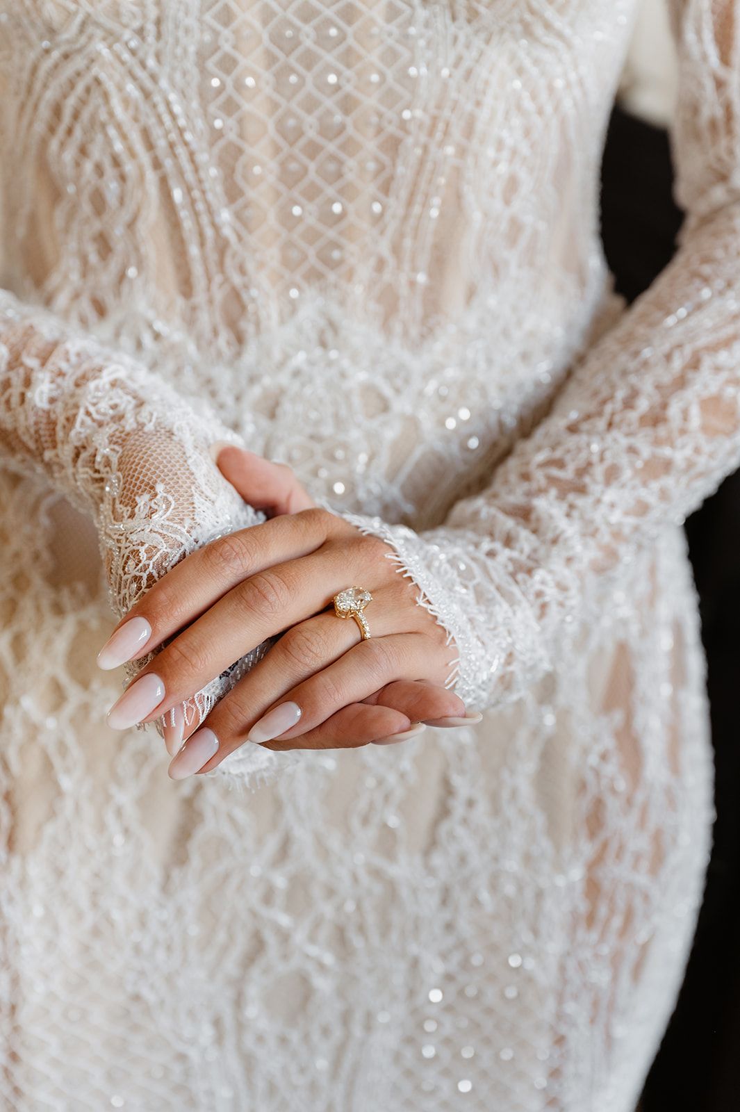 Close-up of bride's hands showing wedding ring and lace sleeve details.