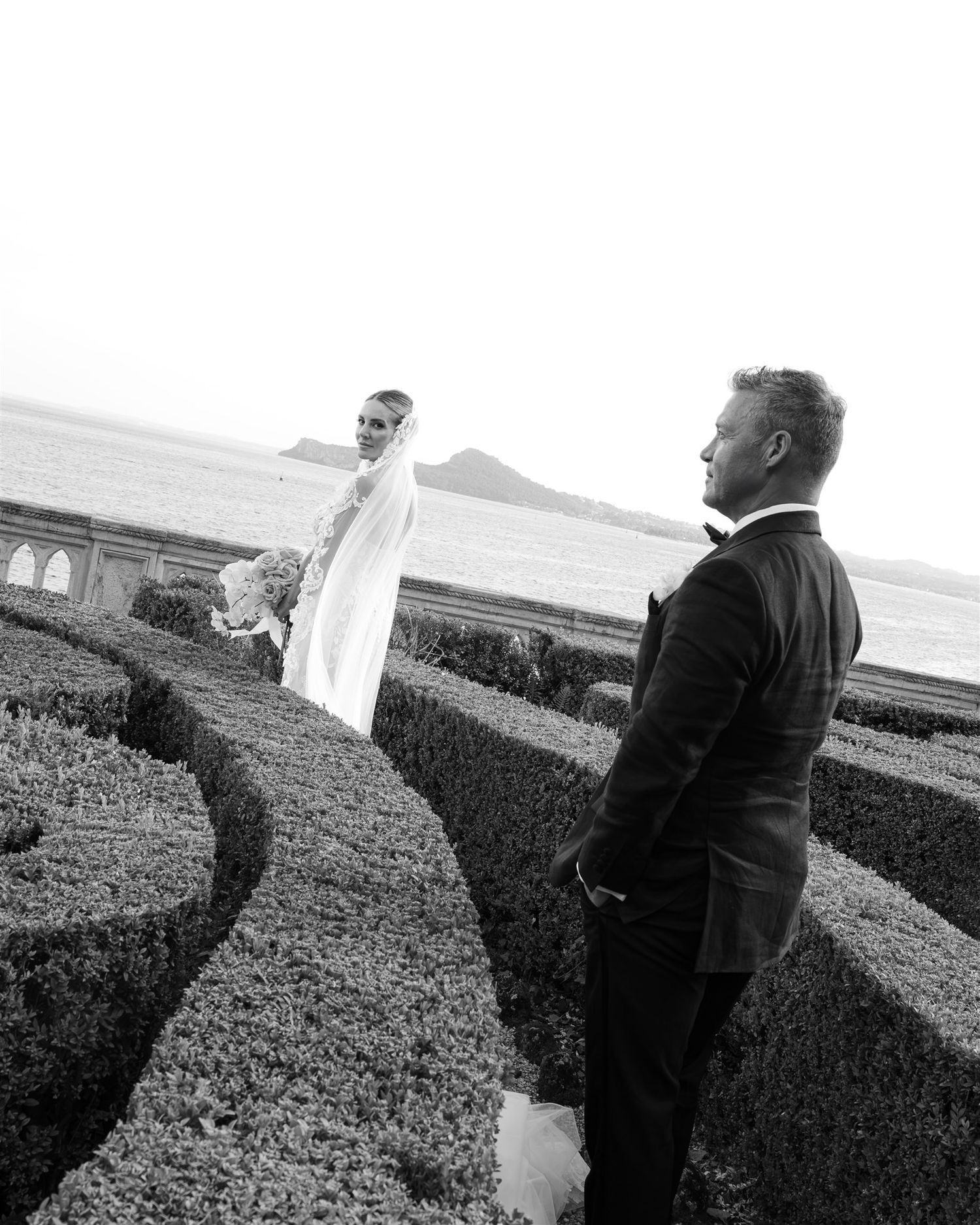 A black and white photo of a couple standing together in an outdoor garden setting.