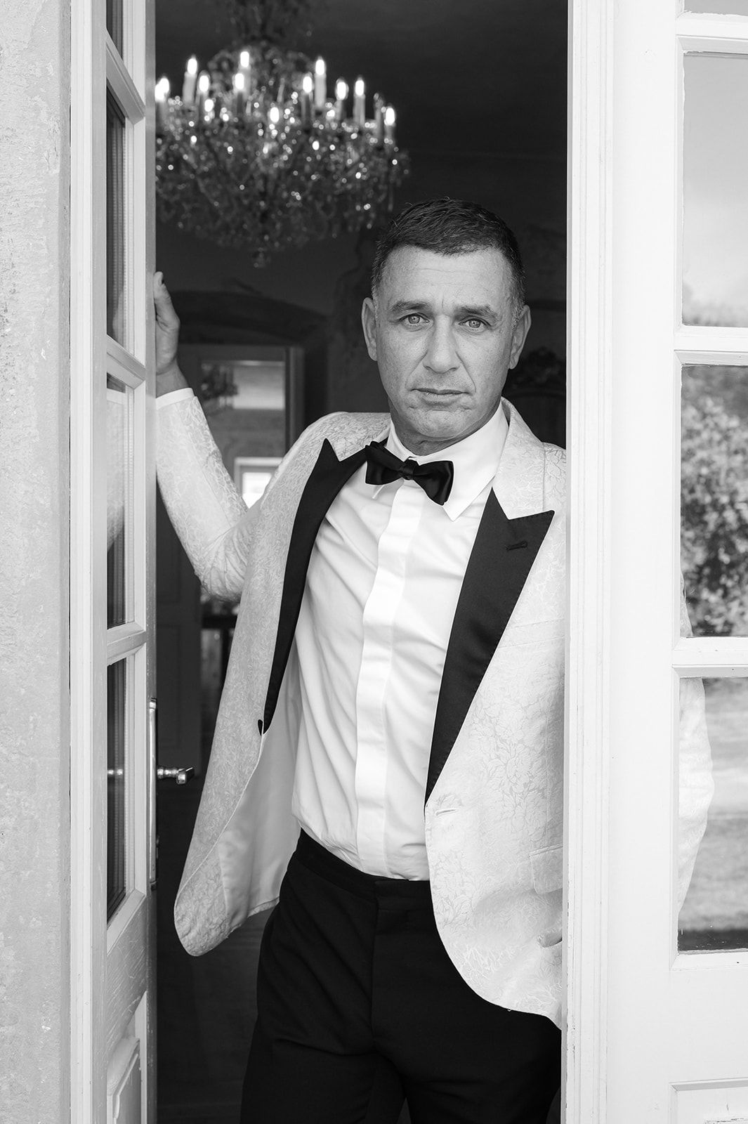 Black and white portrait in formal attire against an elegant interior backdrop.