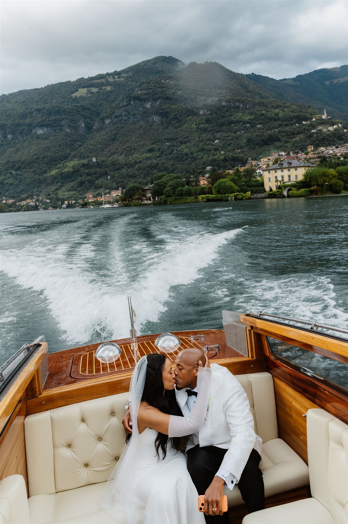 Couple sharing intimate moment on luxury wooden boat with Italian lake scenery.