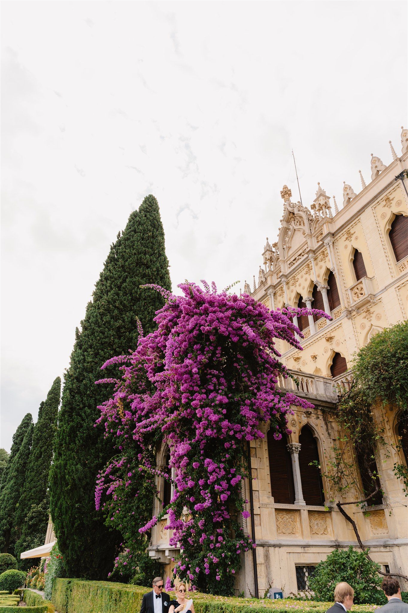 Elegant Mediterranean villa with blooming purple bougainvillea and cypress trees against white stone architecture.