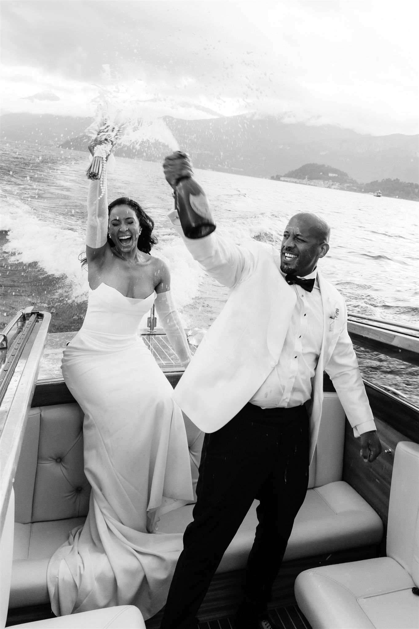 Joyful couple in white attire laughing together on a luxury boat on Lake Como