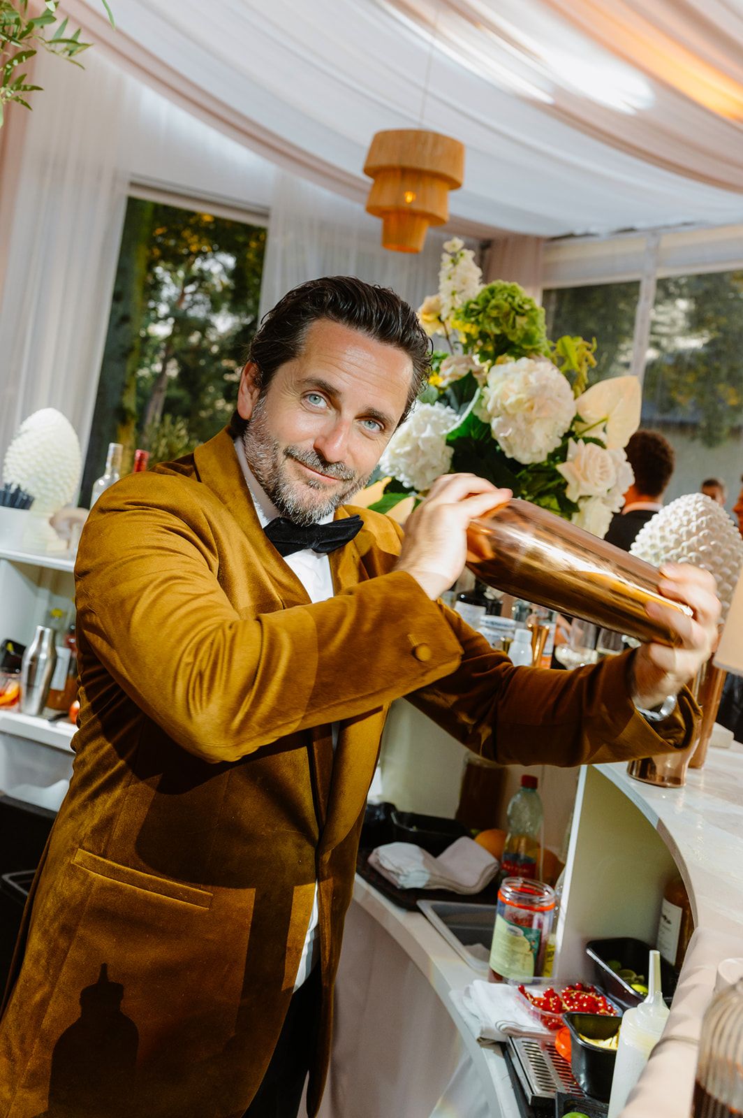 Bartender in brown jacket pouring drinks at elegant wedding reception bar.