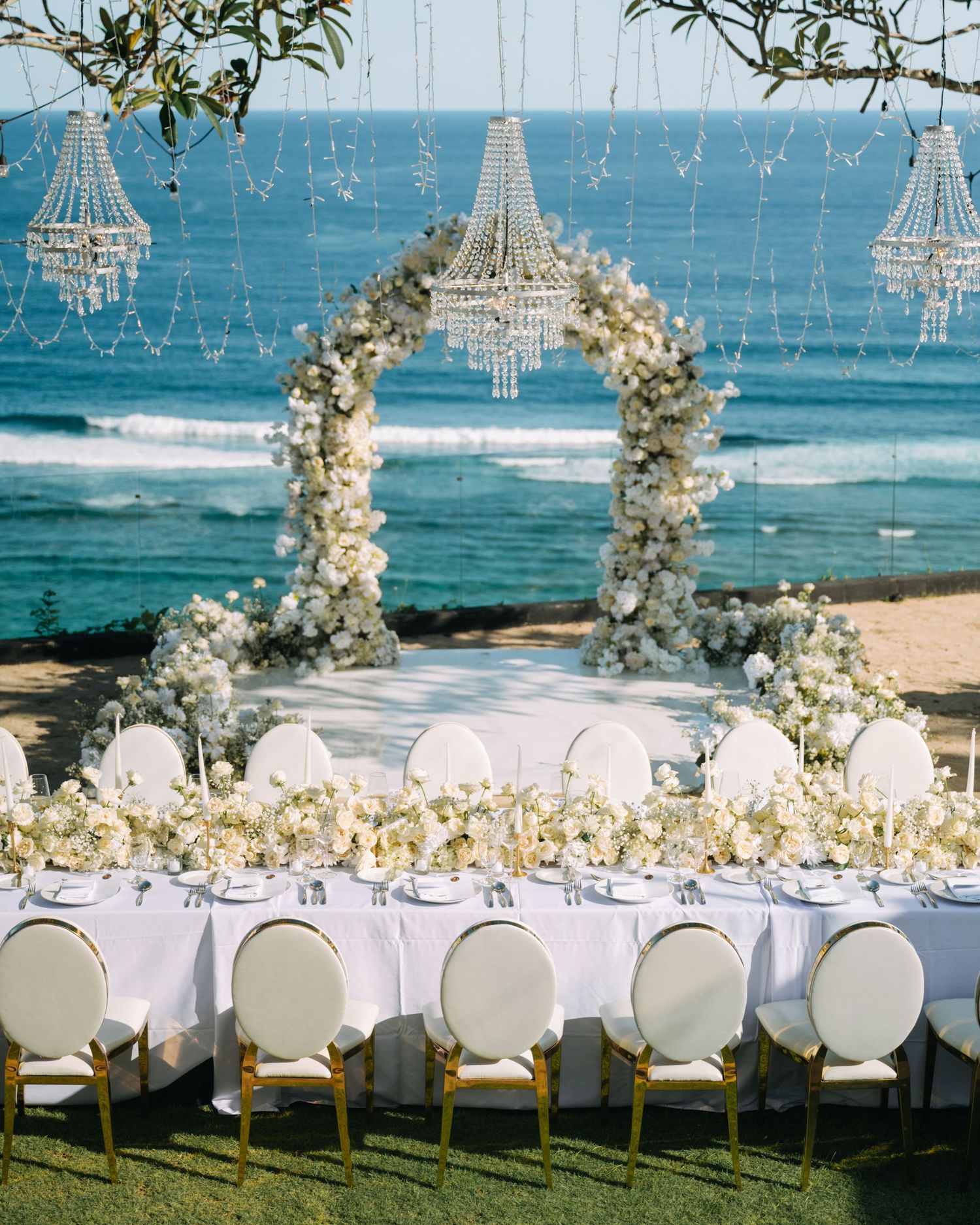 Elegant beach wedding setup with floral arch and crystal chandeliers overlooking the ocean in Bali