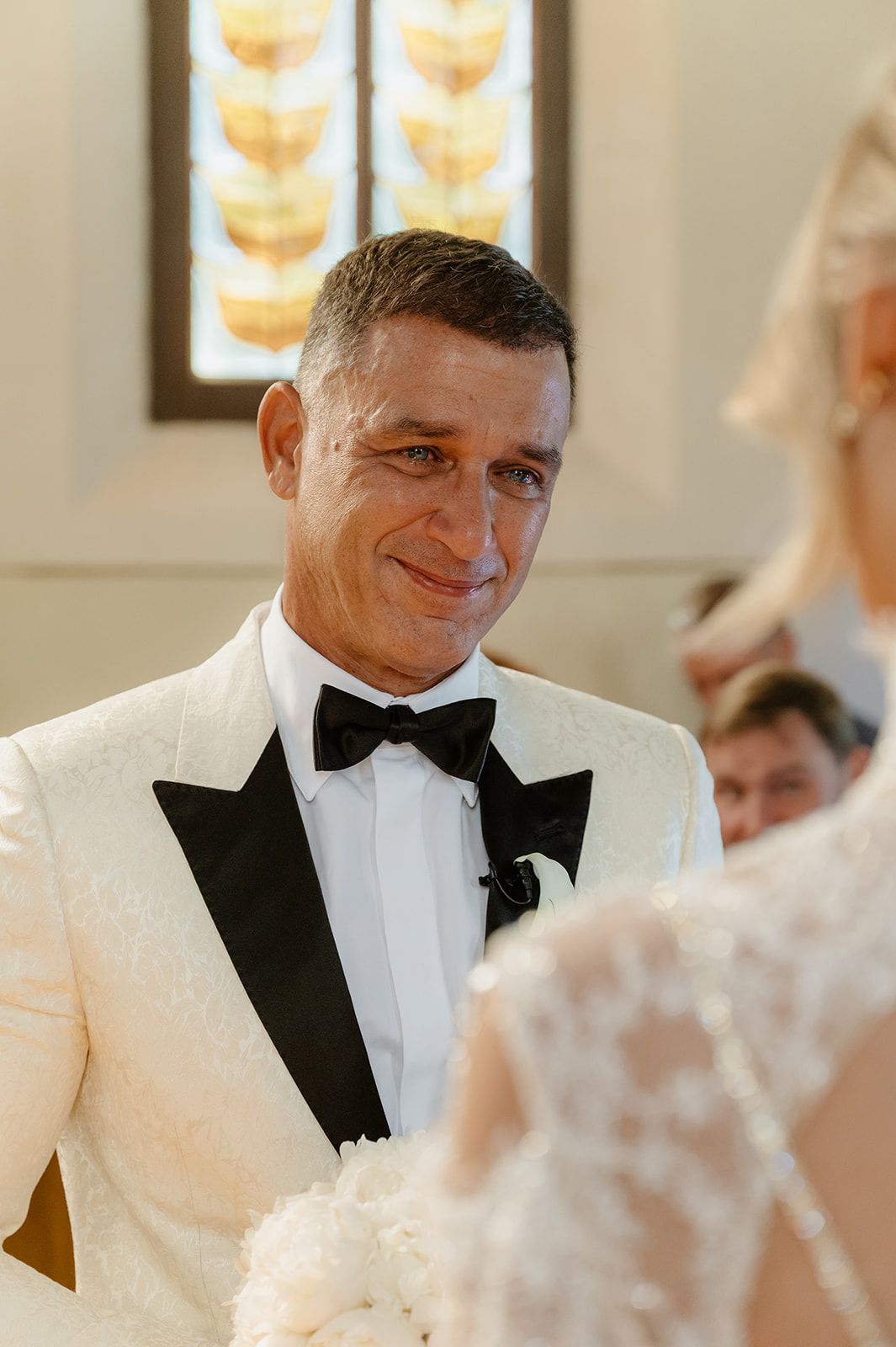 Candid moments of a groom in a white tuxedo jacket and black bow tie during the ceremony.