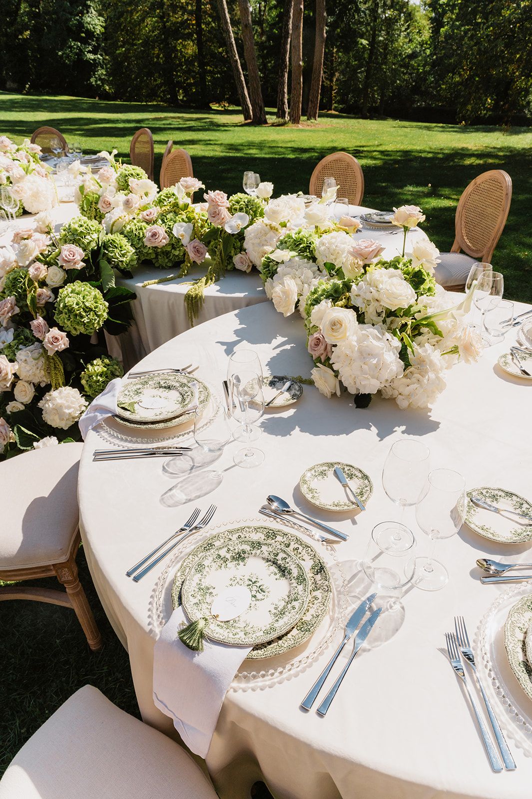 Elegant outdoor wedding reception tables decorated with white floral centerpieces and fine china place settings.