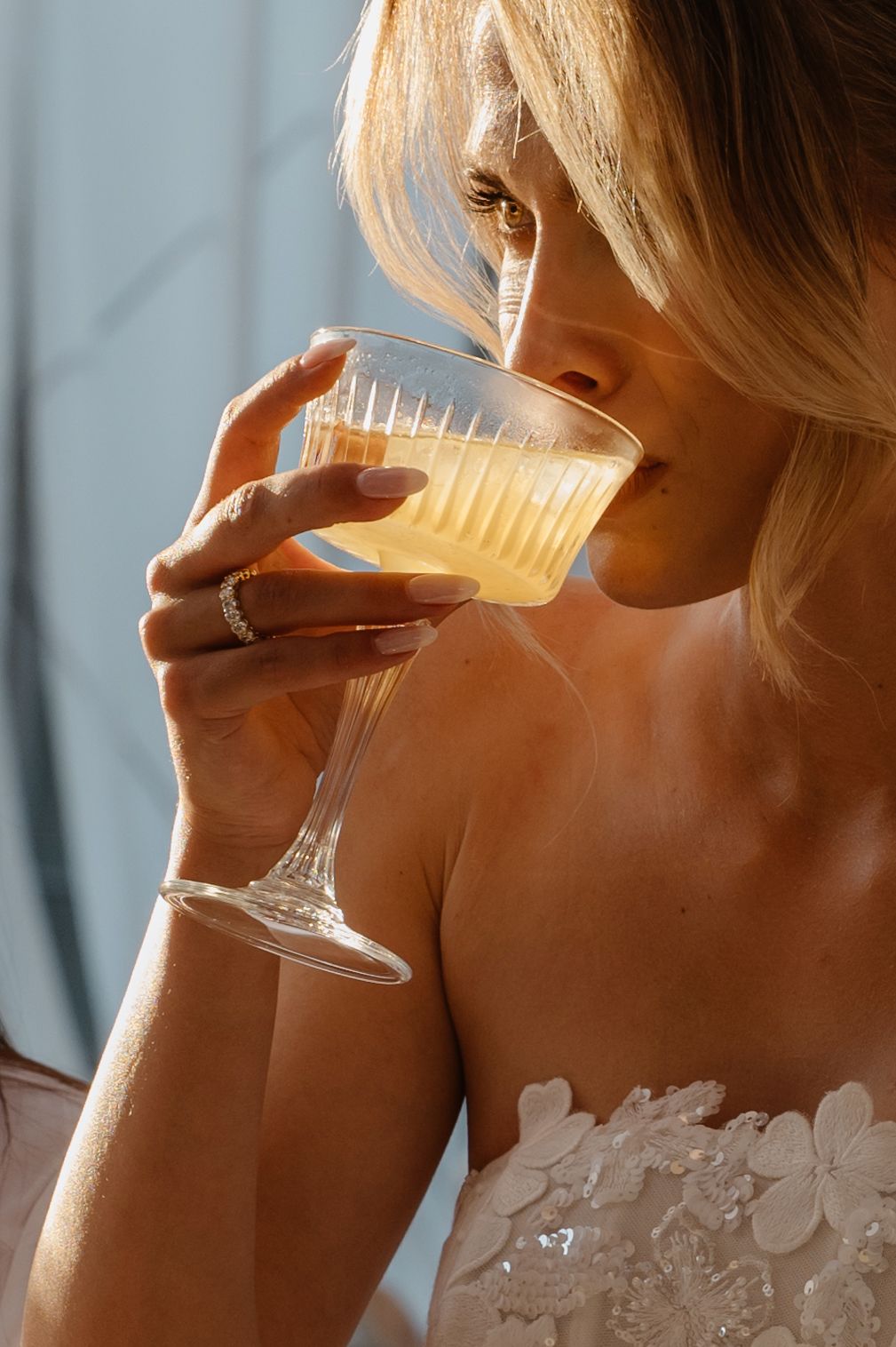 Close-up of champagne glass being sipped with lace dress detail visible.