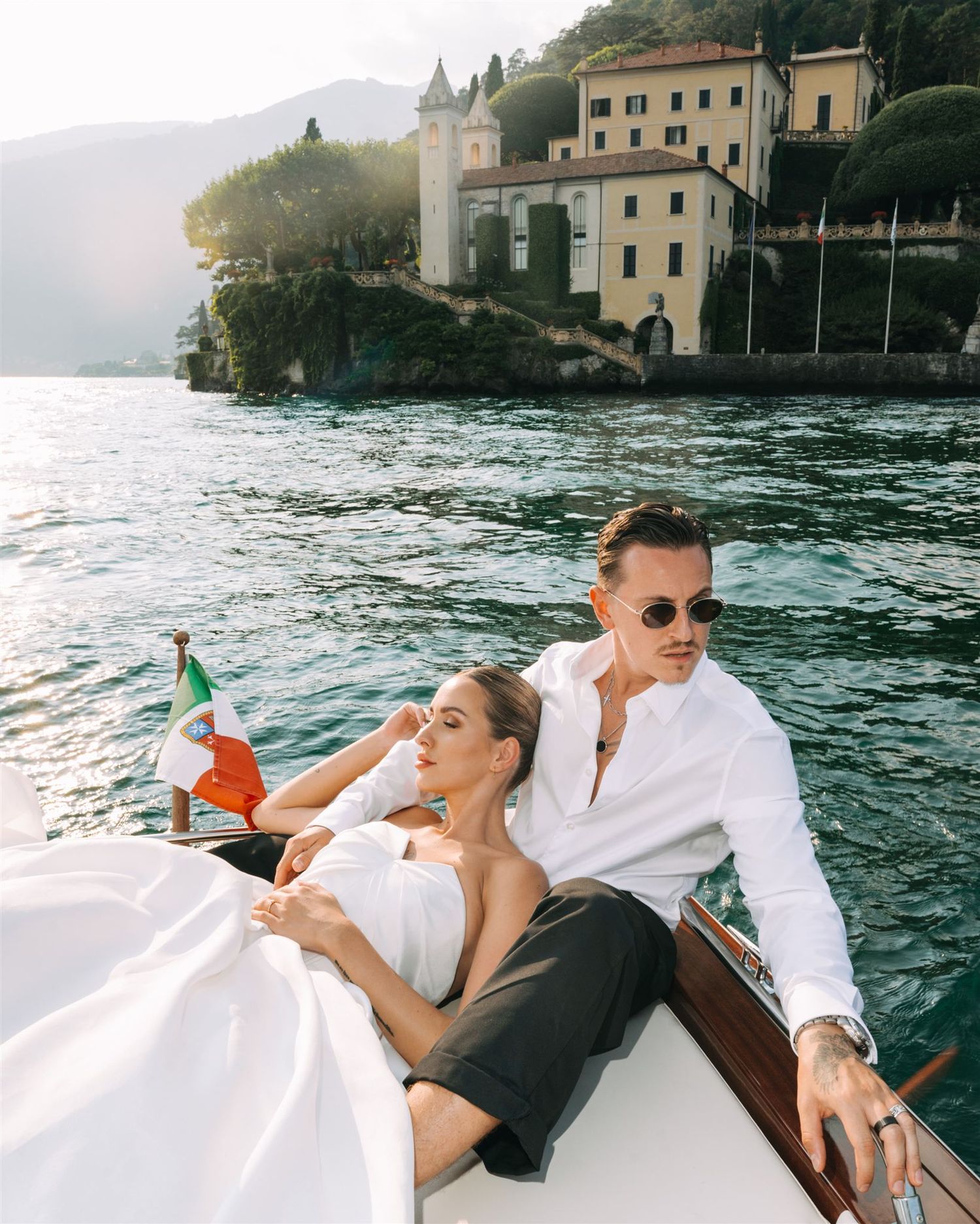 Couple relaxing on a luxury boat along the Italian coastline with historic villas visible in the background.