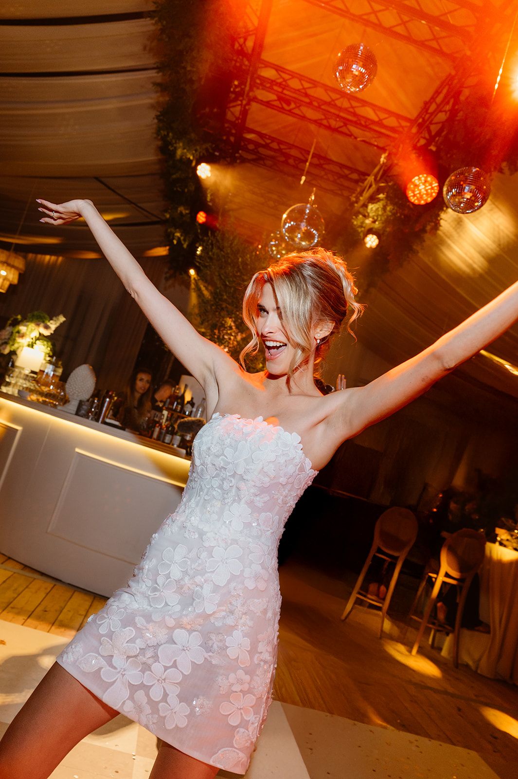 Celebratory dance moves in a white textured dress under warm reception lighting.