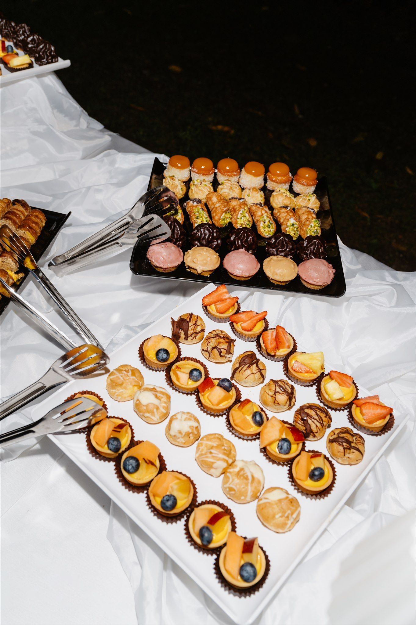 Elegant display of miniature desserts and pastries on white tablecloths.