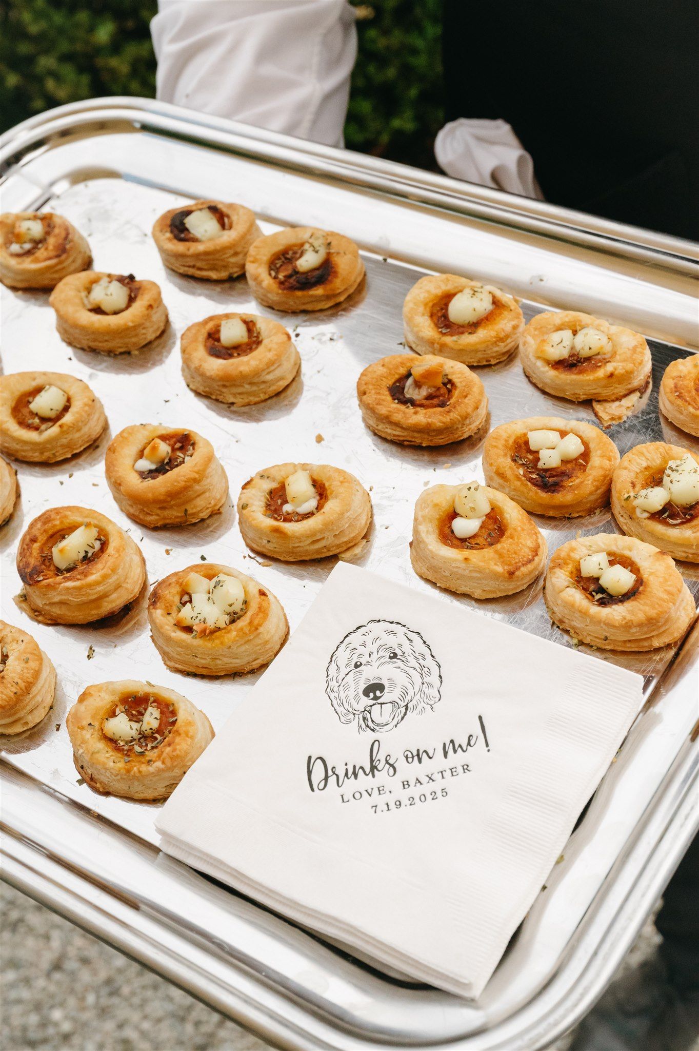 Appetizer tray of gourmet pastries with custom wedding branding on serving paper.