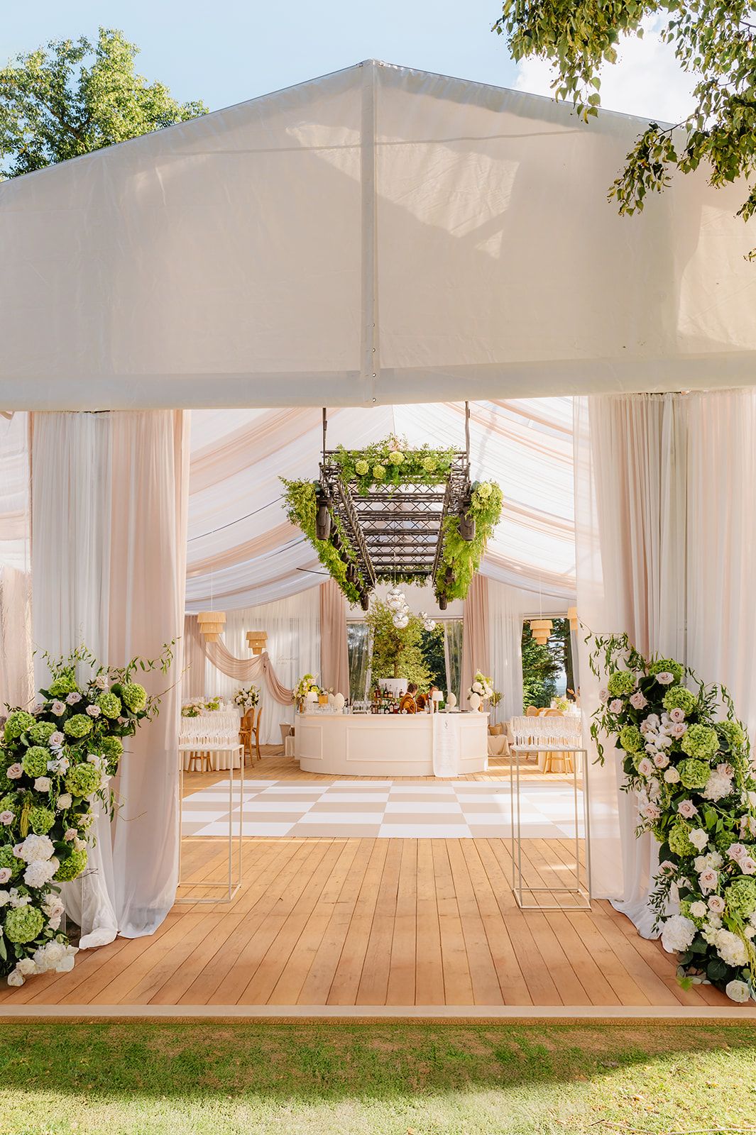 White draped tent pavilion with wooden flooring and floral arrangements for an outdoor wedding.