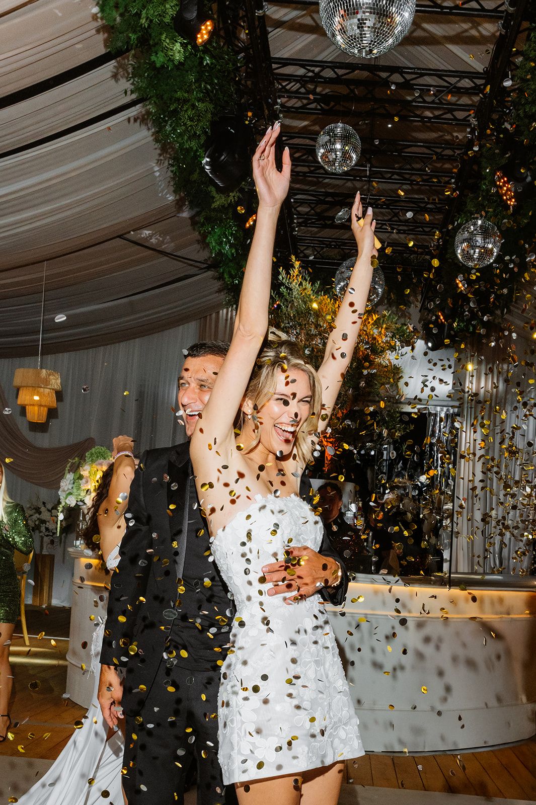 Joyful celebration with confetti falling under a disco ball in an elegant white tent venue.