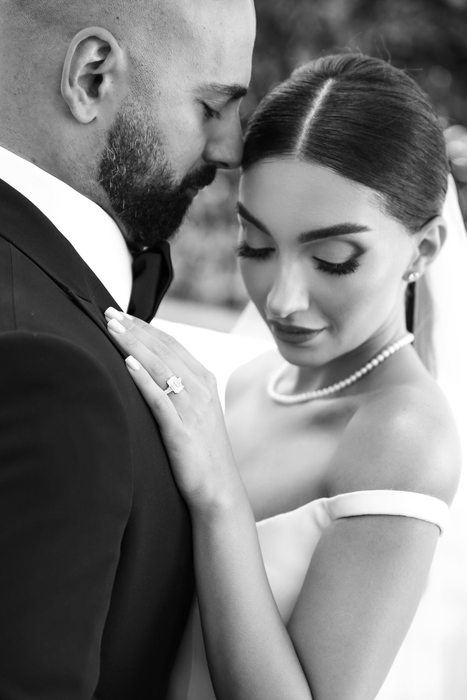 Black and white wedding portrait of bride and groom sharing an intimate moment, bride wearing pearl necklace and diamond ring.