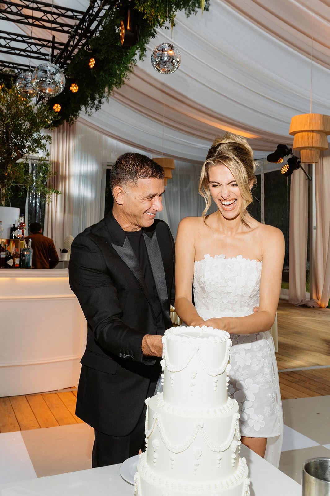 Wedding couple sharing playful moment while cutting their white tiered cake.