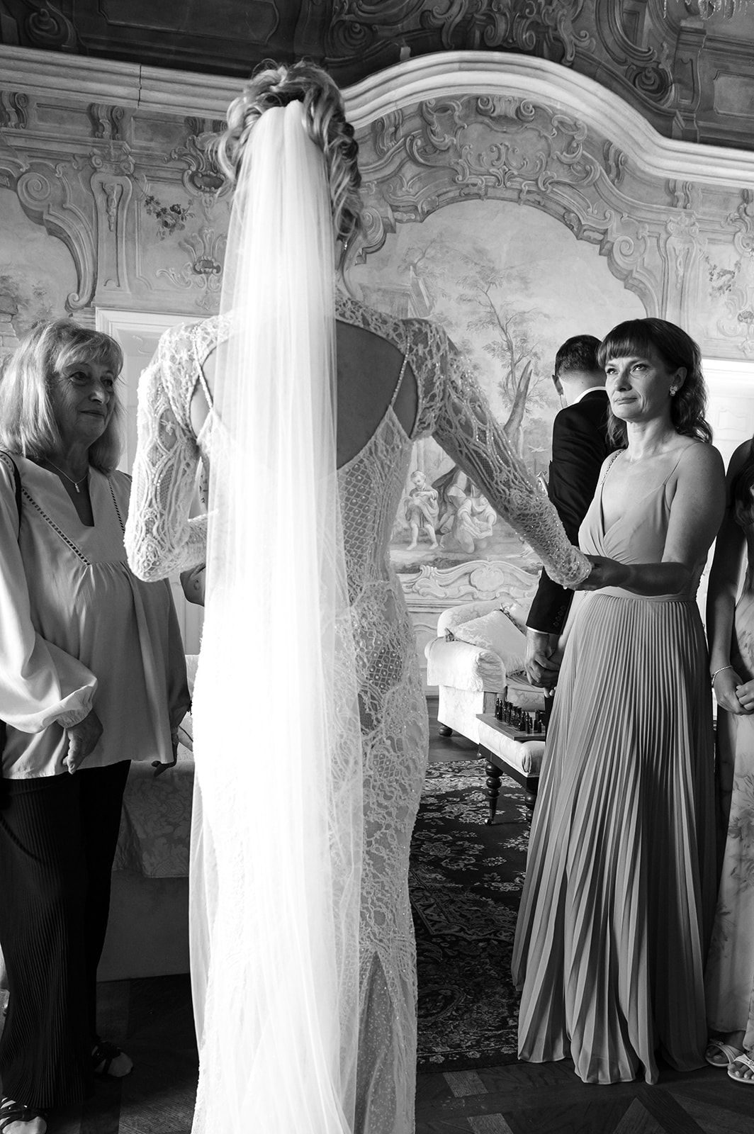 Black and white photo of wedding guests in formal attire mingling in an ornate room with decorative walls.