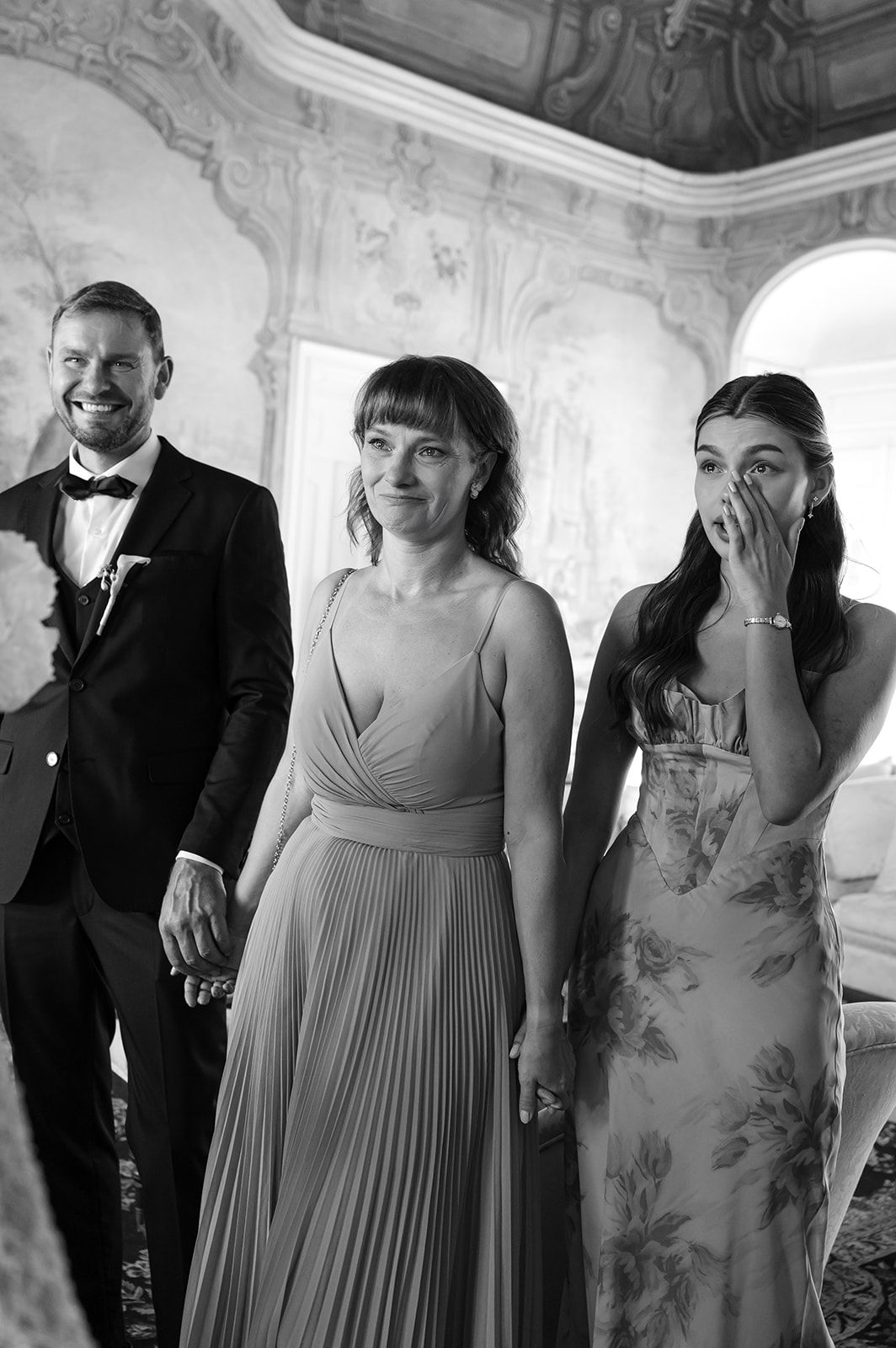 Wedding party members in formal attire gathered in an elegant room with ornate wall decorations.