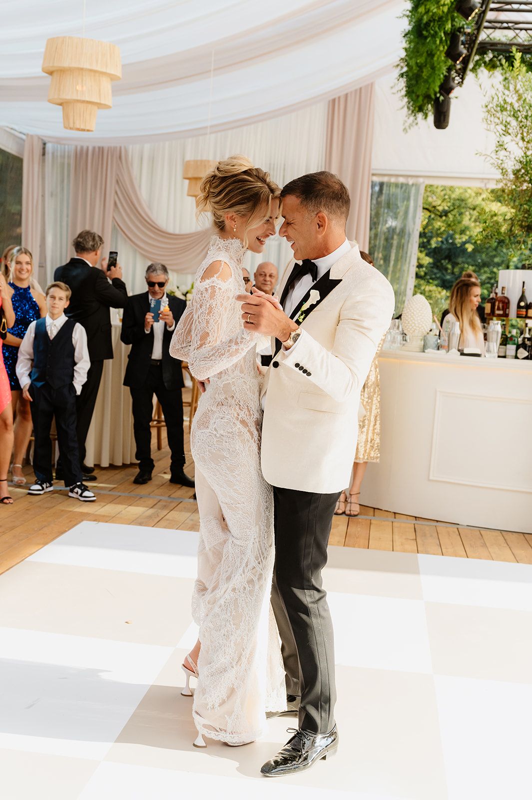 Elegant couple dancing on a white dance floor under draped fabric at a wedding reception.