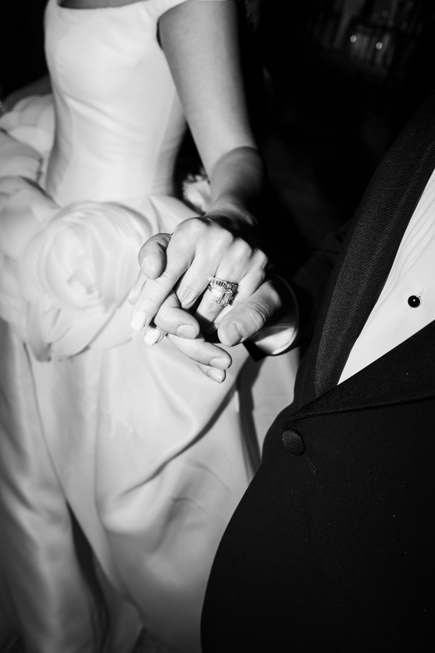 Black and white wedding photo of bride and groom holding hands, showcasing a sparkling diamond engagement ring.