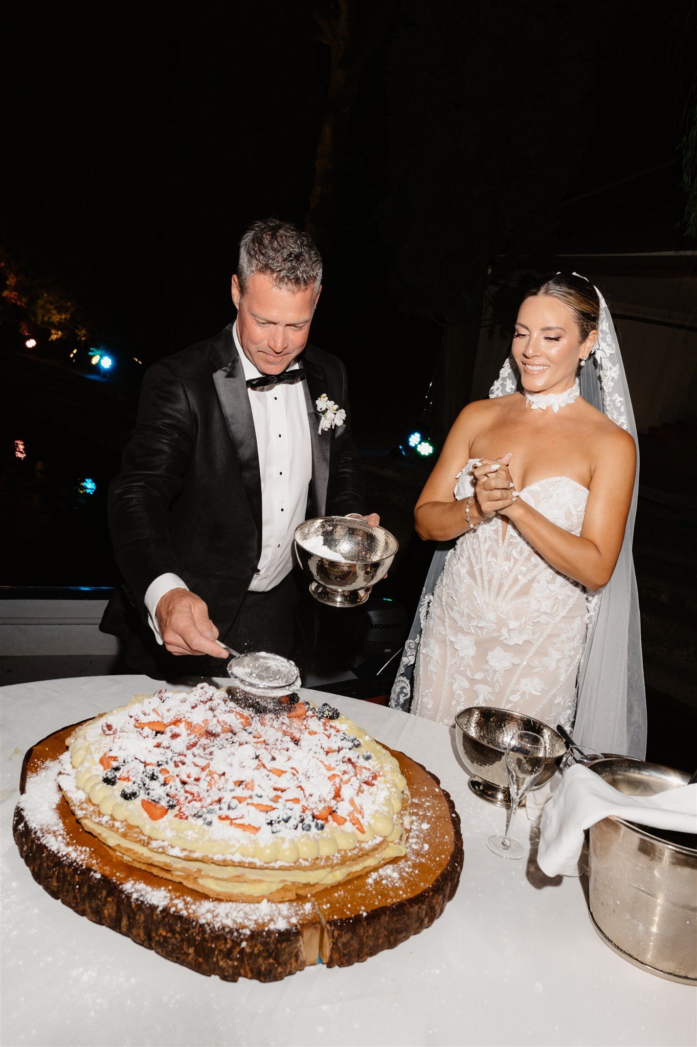 A wedding cake decorated with whipped cream and fresh berries on a wooden platter.