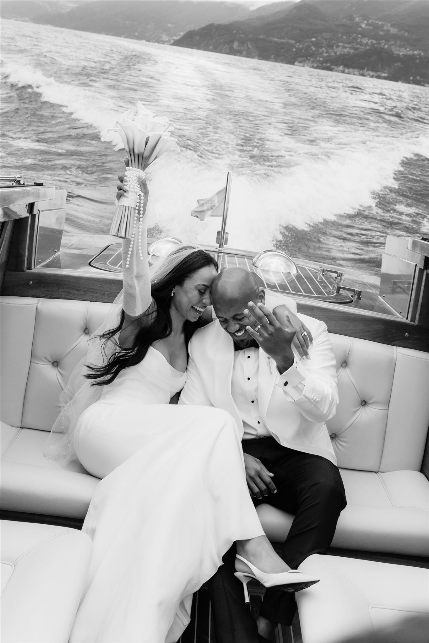 Romantic couple in white formal wear embrace on a boat with scenic mountain views on Lake Como