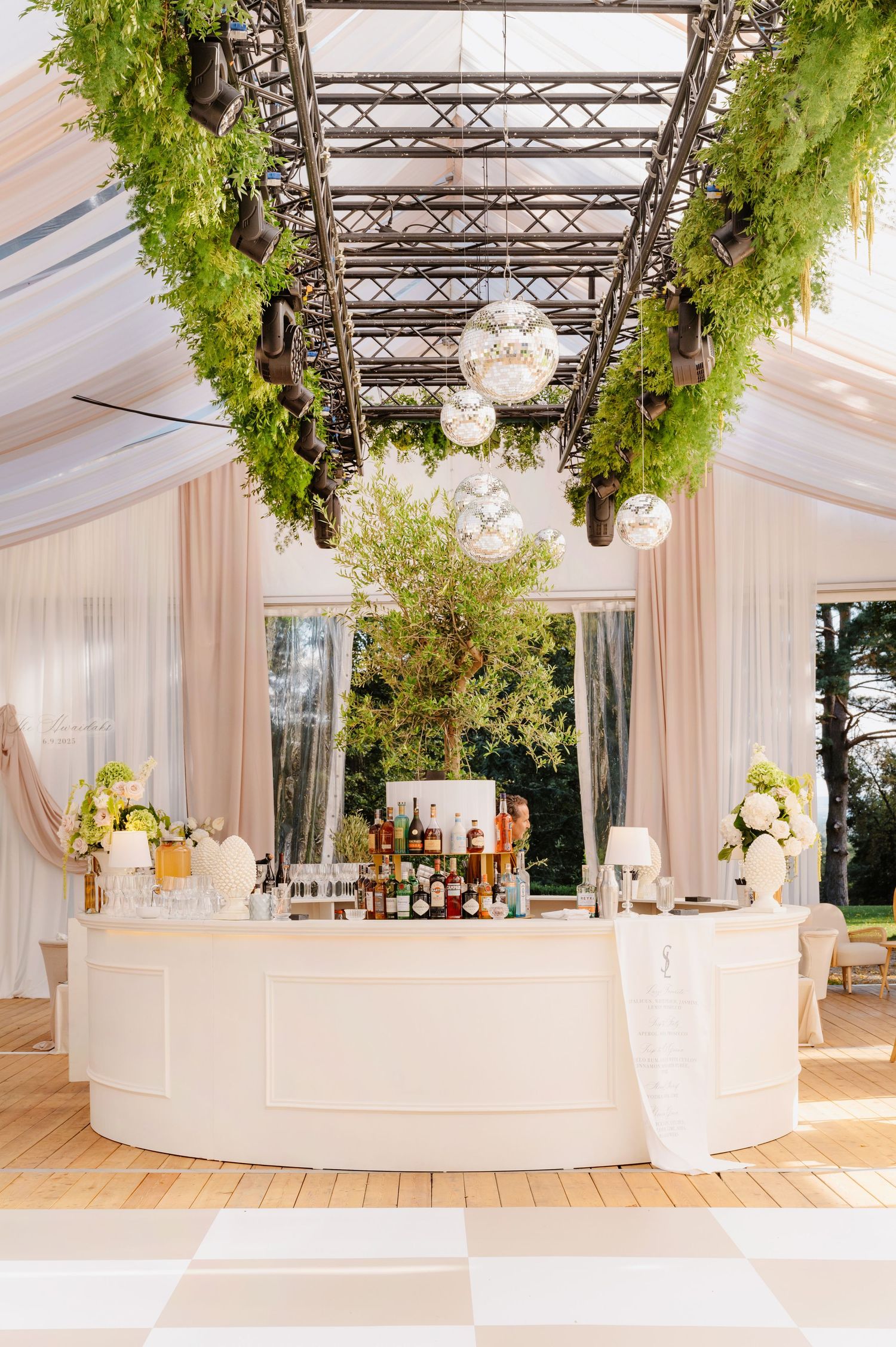 Elegant white tent reception venue with hanging greenery and curved bar setup.