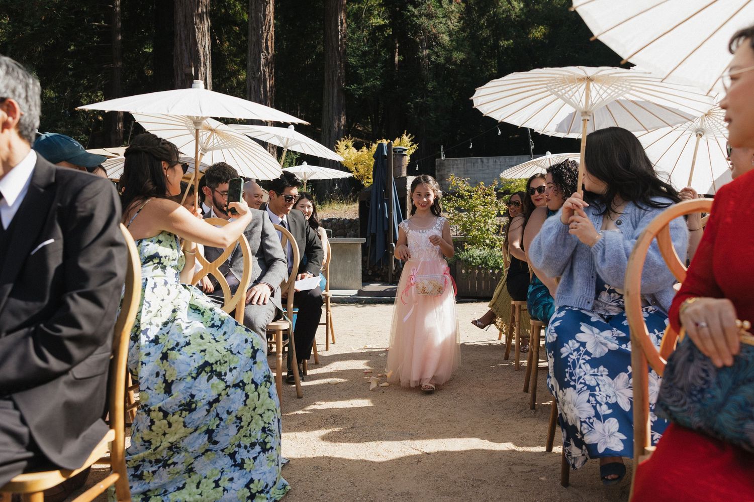 A crowd gathers outdoors under white paper parasols during a sunny daytime event.