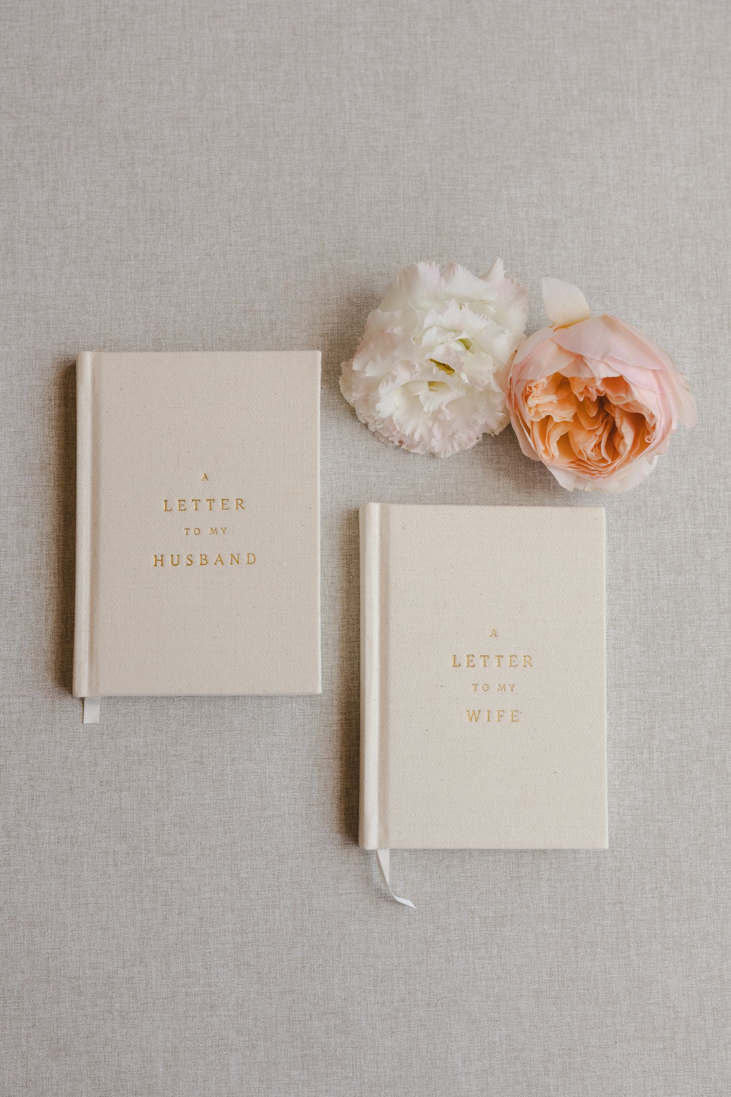 Two minimalist wedding vow books with white and peach roses on linen background.