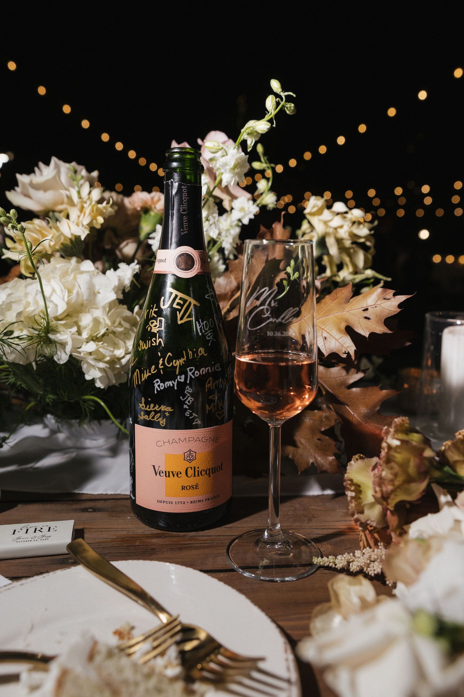 Elegant wedding reception table with champagne bottles, floral arrangements and string lights creating a romantic ambiance.