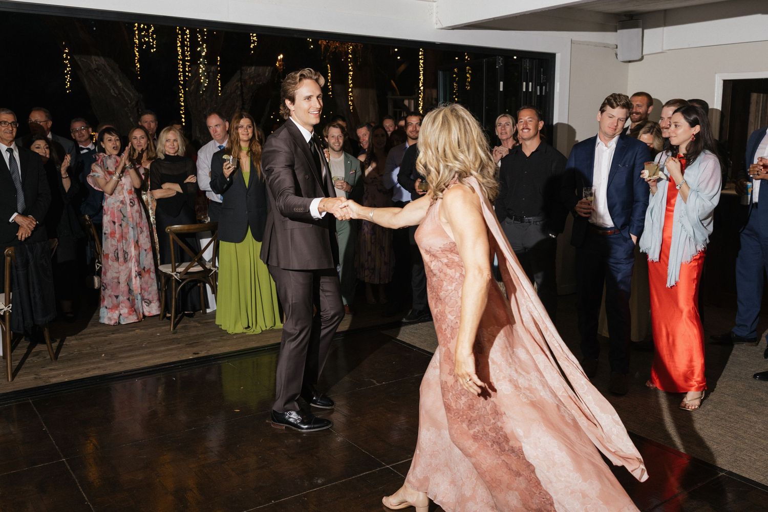 Couple dancing energetically on wedding reception dance floor surrounded by elegantly dressed guests.