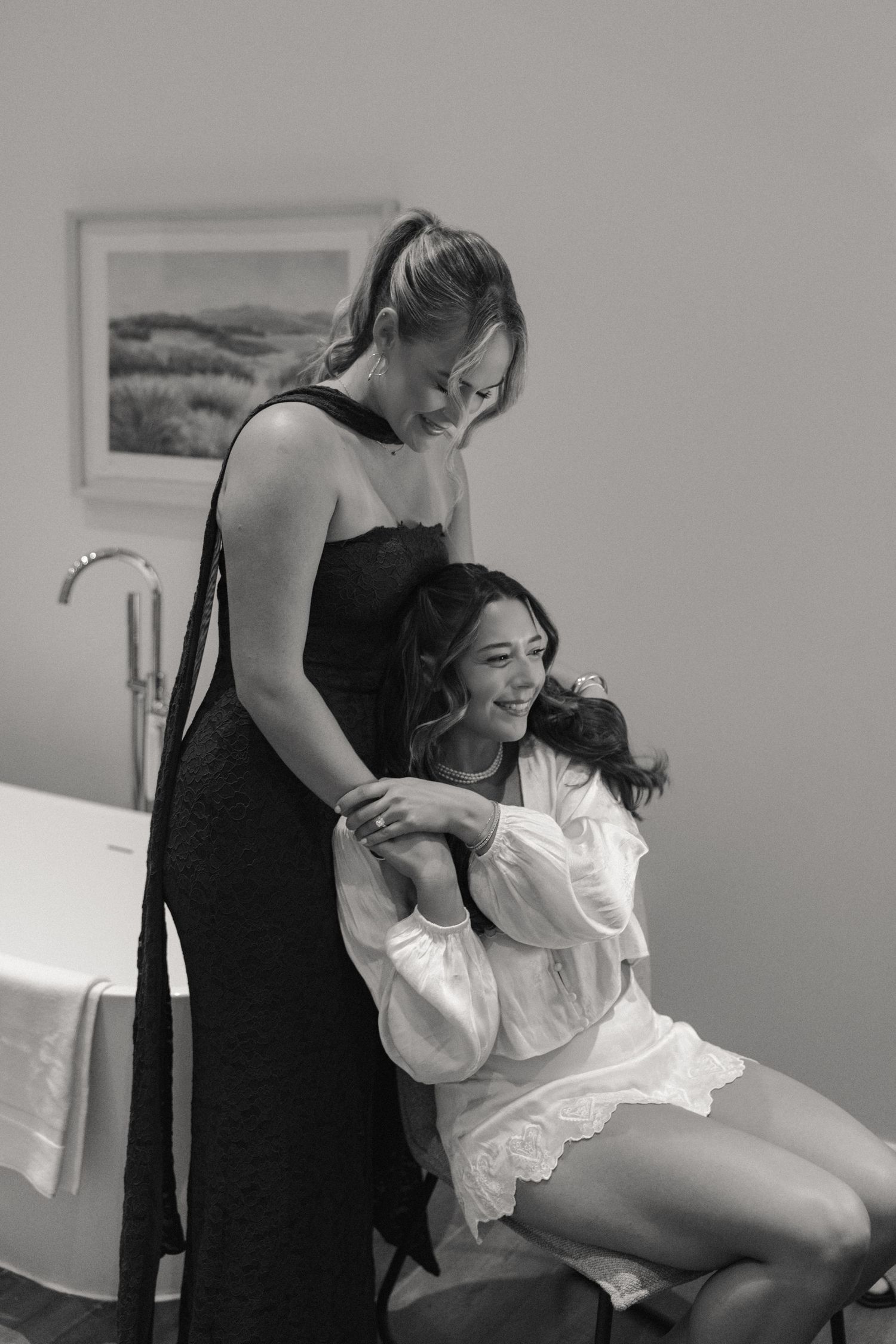 Black and white photo of bride laughing with bridesmaid while getting ready before wedding ceremony.