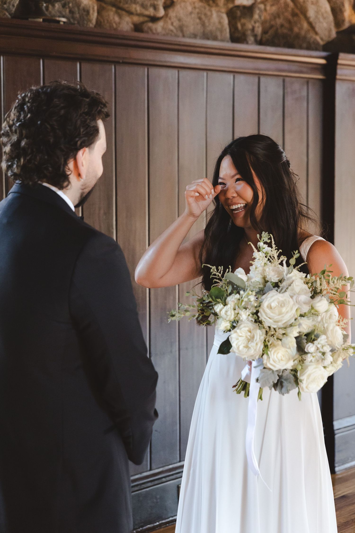 A joyful candid moment during a wedding ceremony features a bride in white holding a lush bouquet of white flowers.