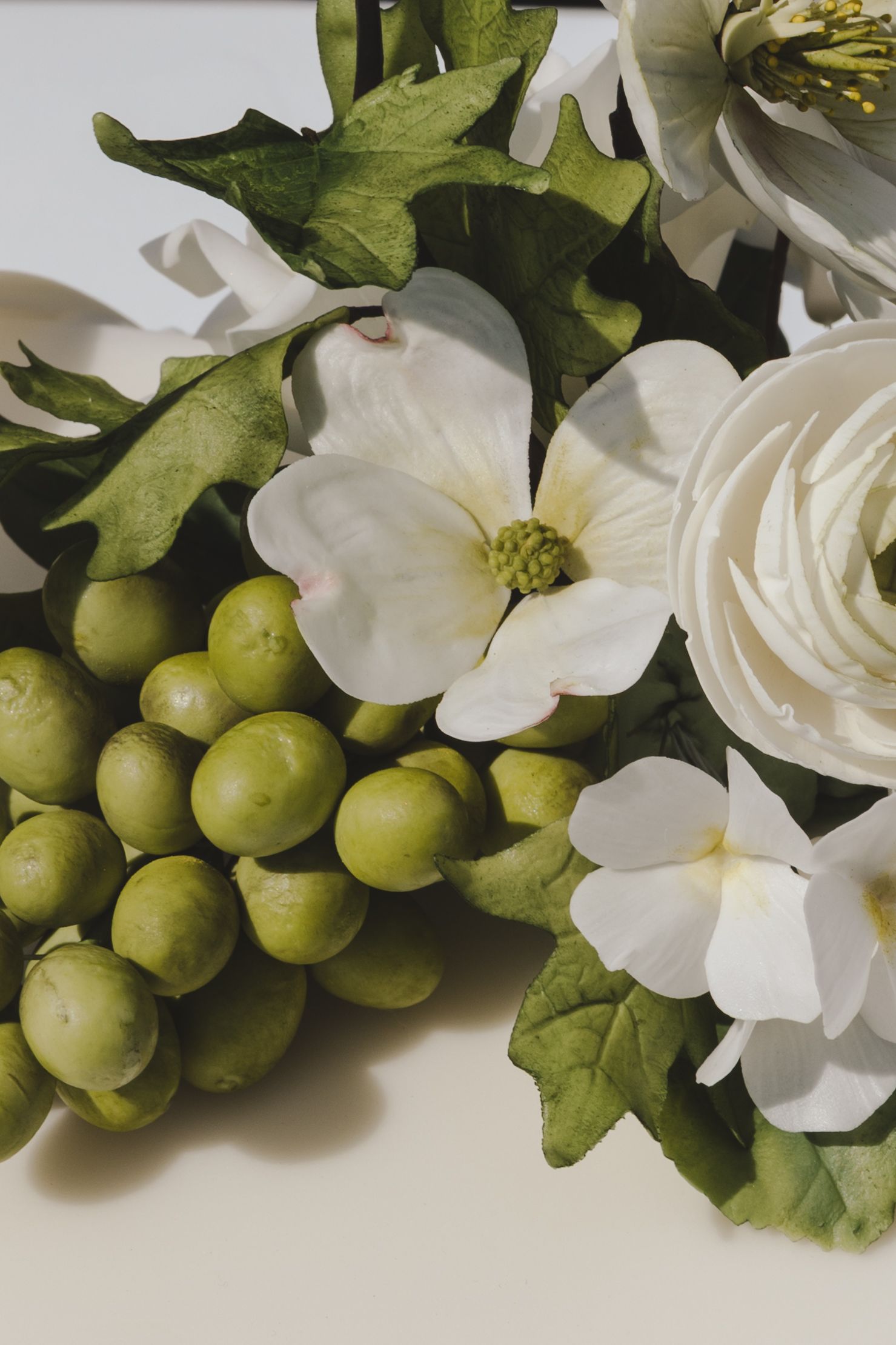 Elegant white dogwood blooms and roses arranged with fresh green grapes and leaves on white background.