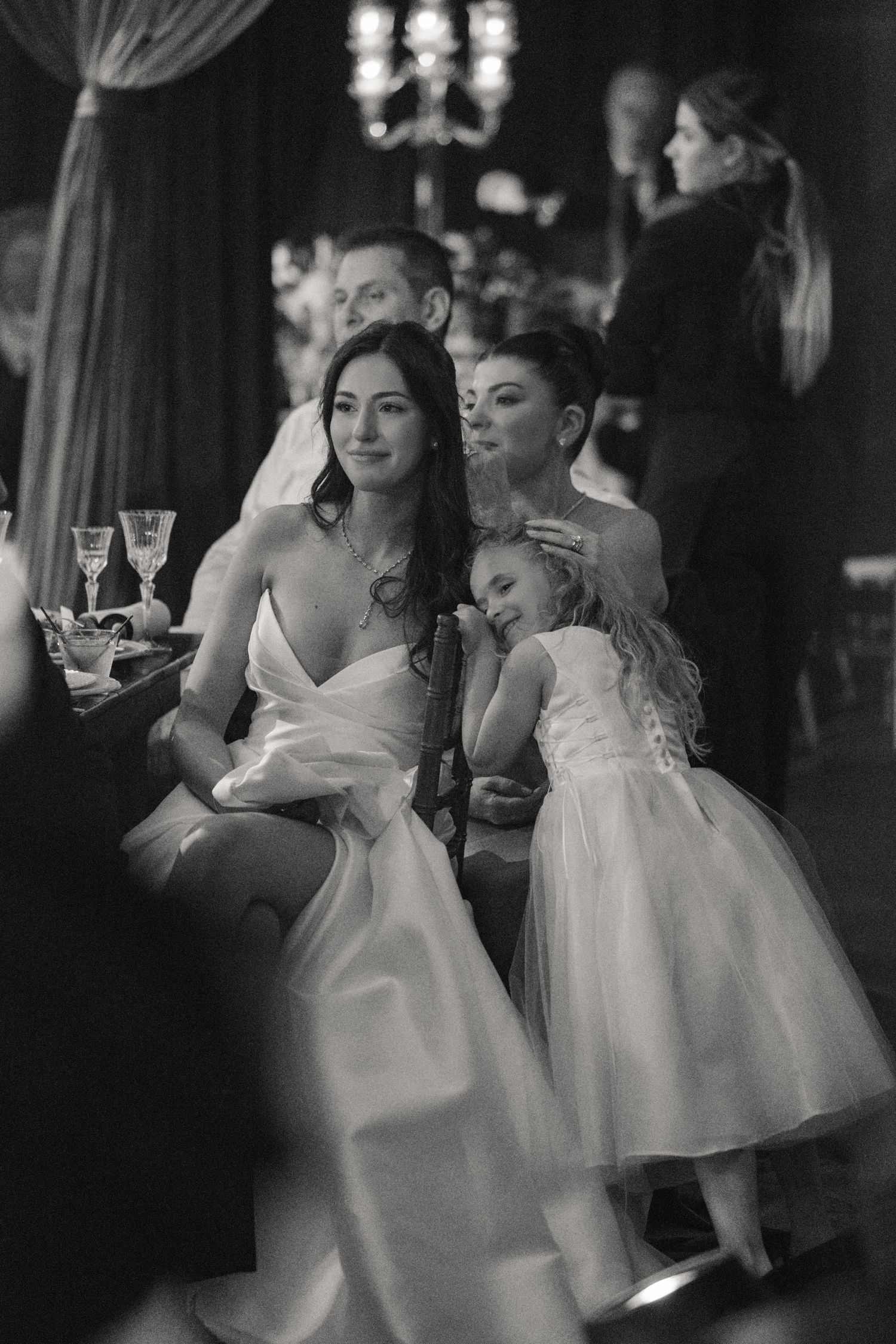 Black and white photo of bridesmaids in elegant white dresses holding champagne glasses at a wedding reception.