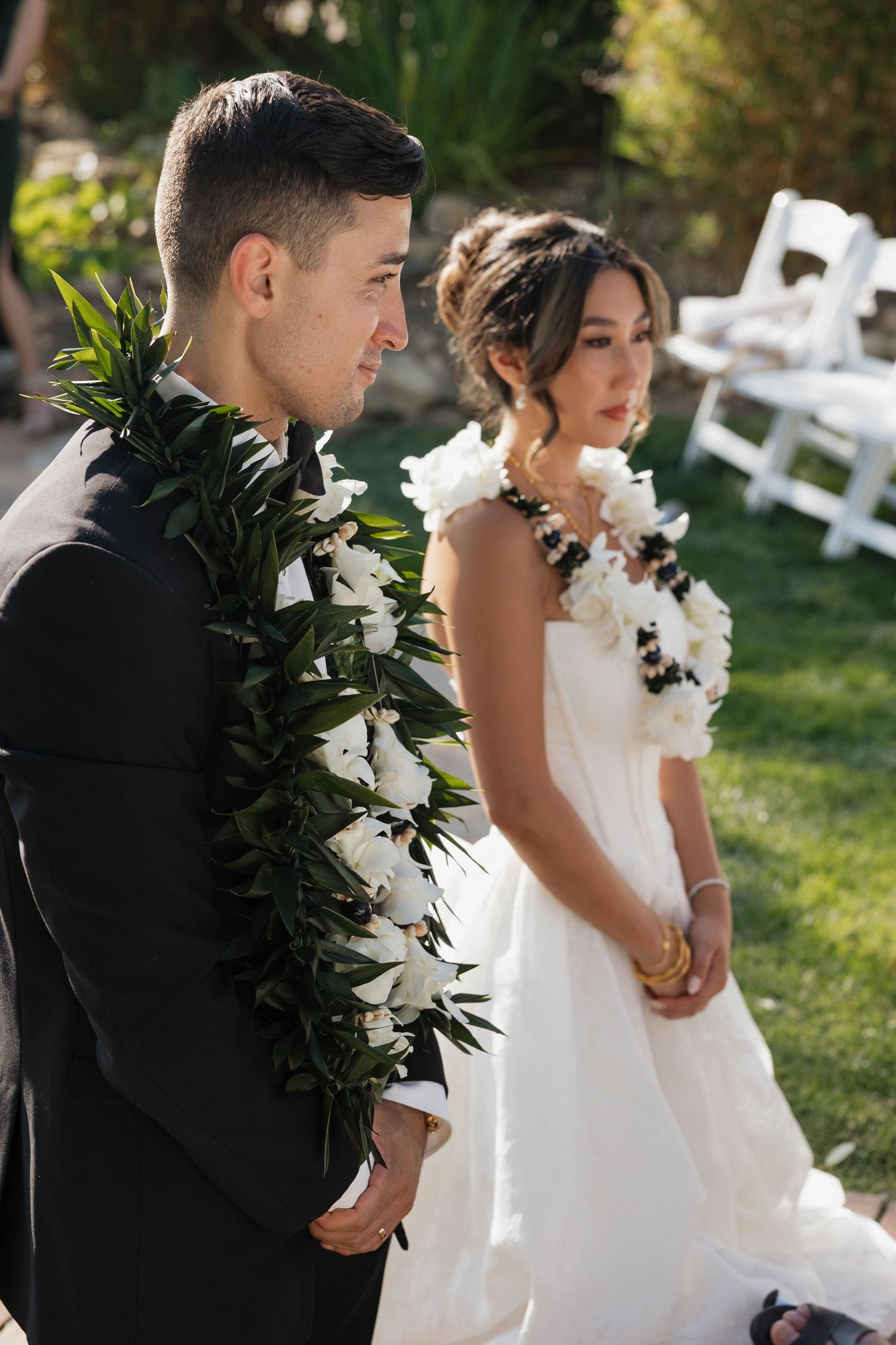 Wedding party members carry white floral arrangements while walking through garden ceremony space.