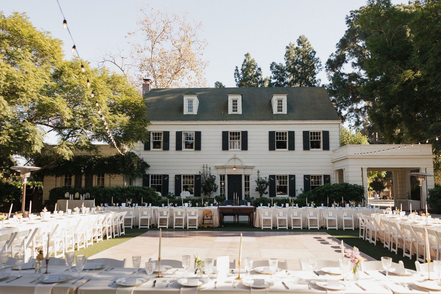 Panoramic view of a classic white colonial style house with black shutters and outdoor wedding ceremony setup.