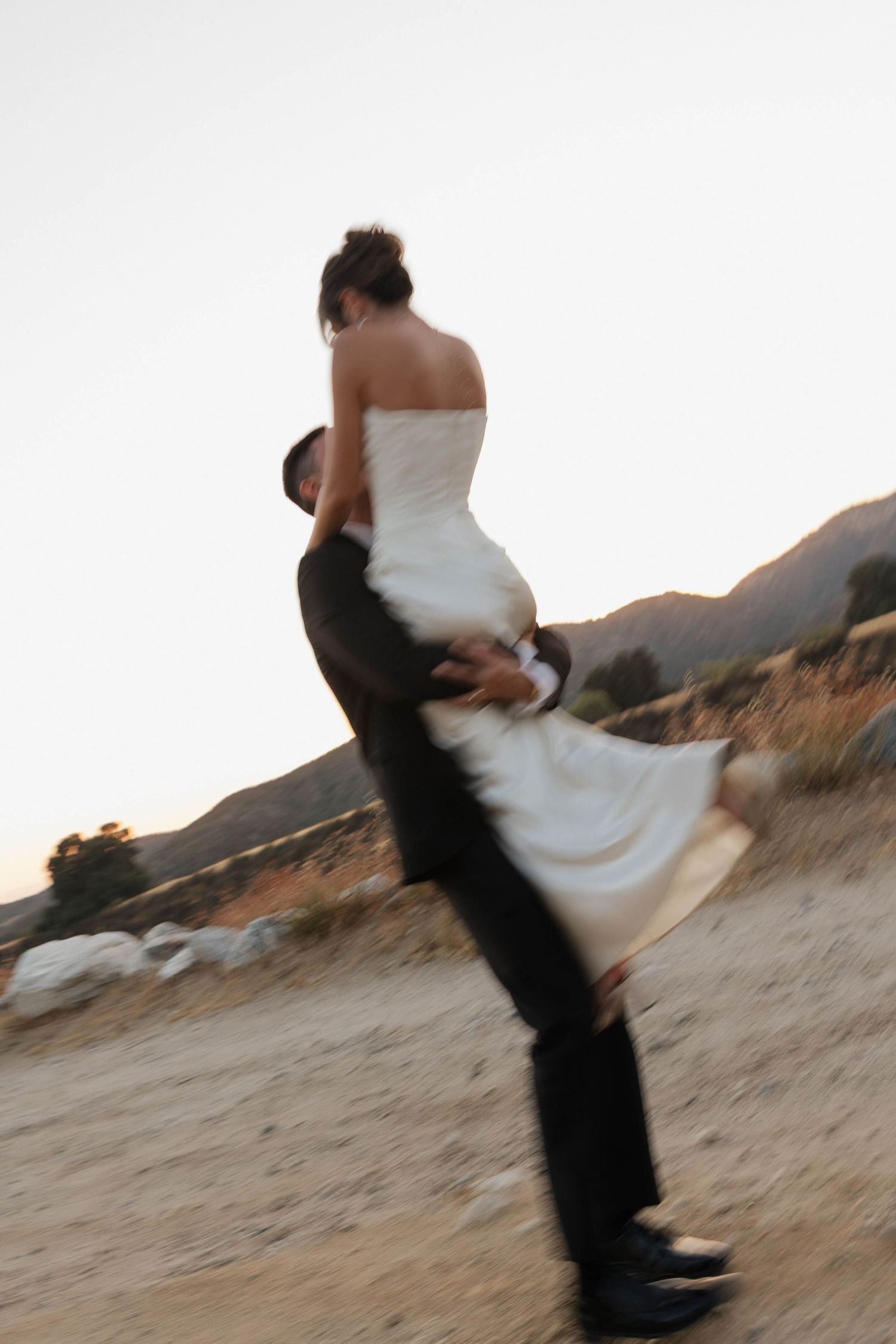 Motion-blur capture of groom lifting bride in spinning dance move at sunset.