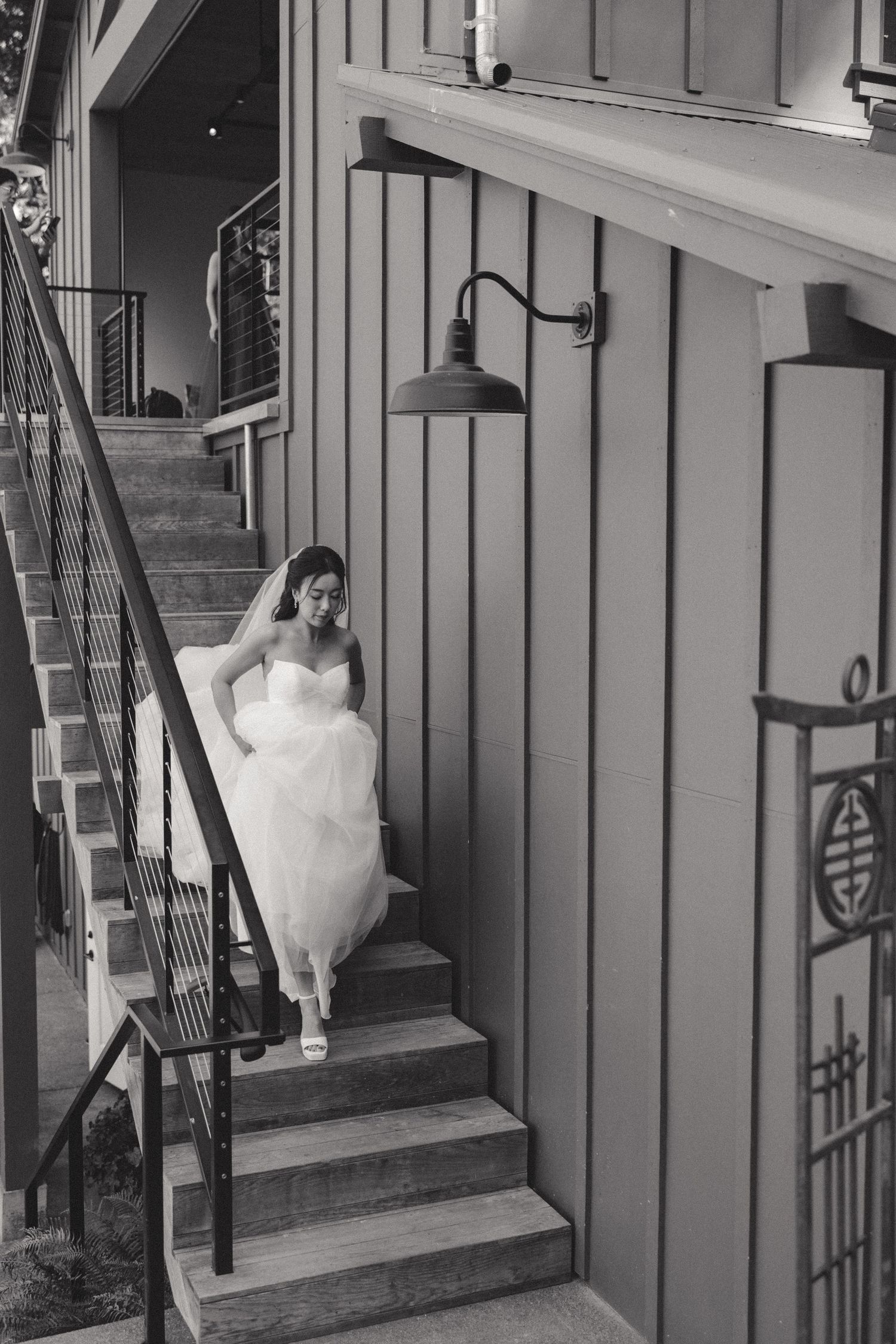 A flowing white wedding dress moves gracefully up wooden stairs in a rustic setting.