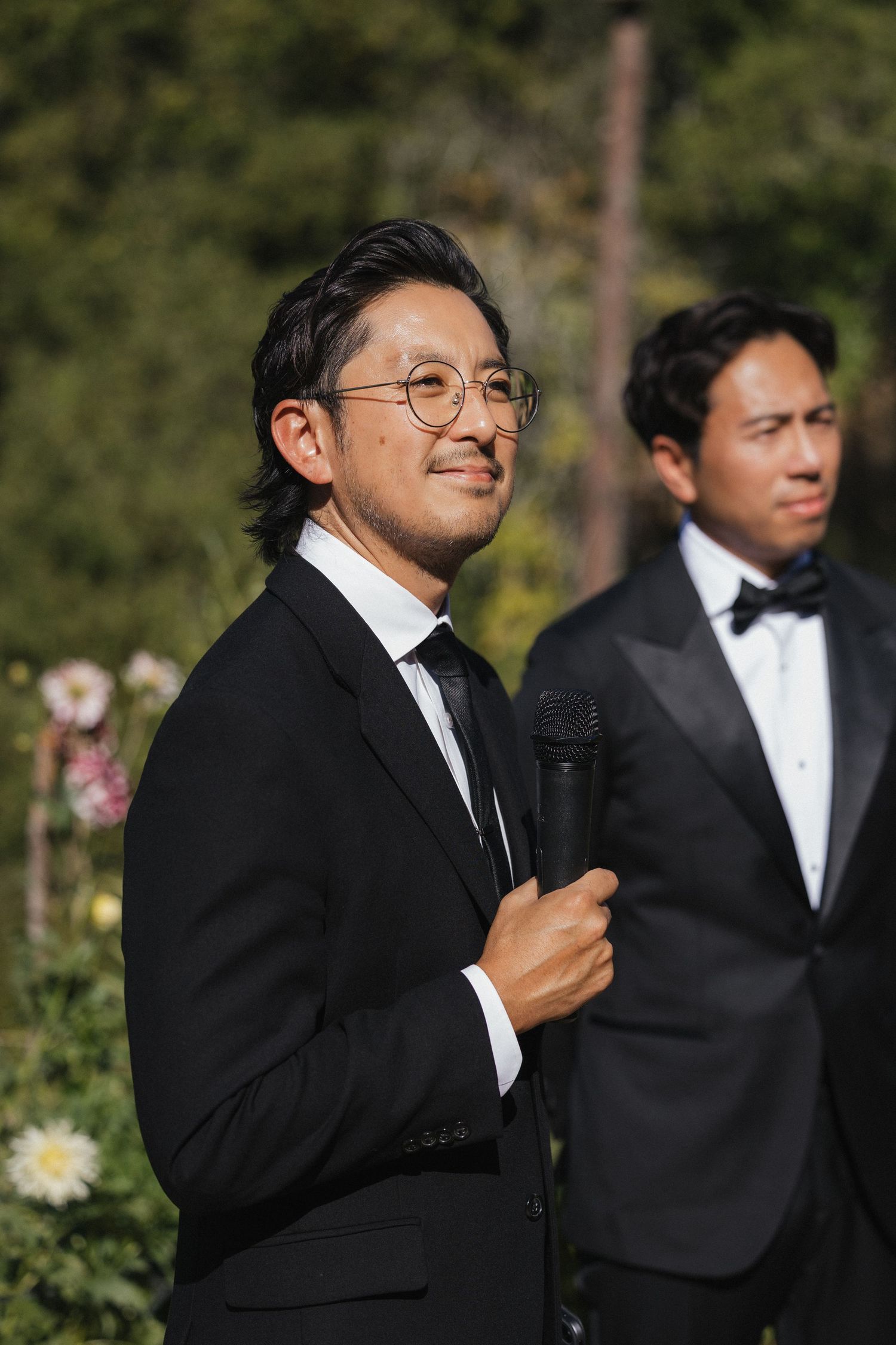 Men in black tuxedos speaking at formal outdoor event.