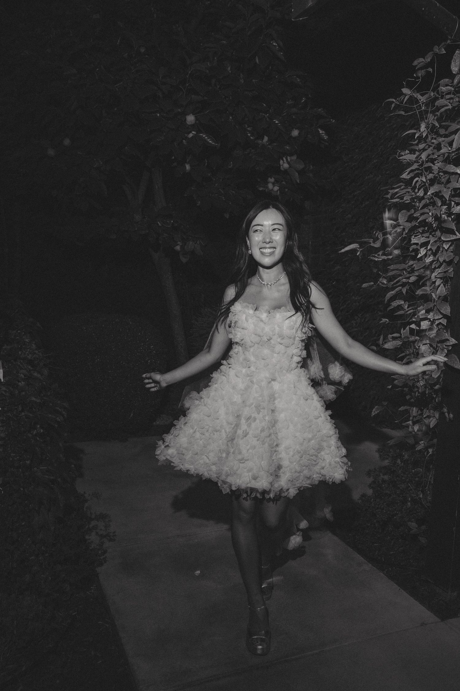 Black and white photo of person twirling in short ruffled party dress outdoors.