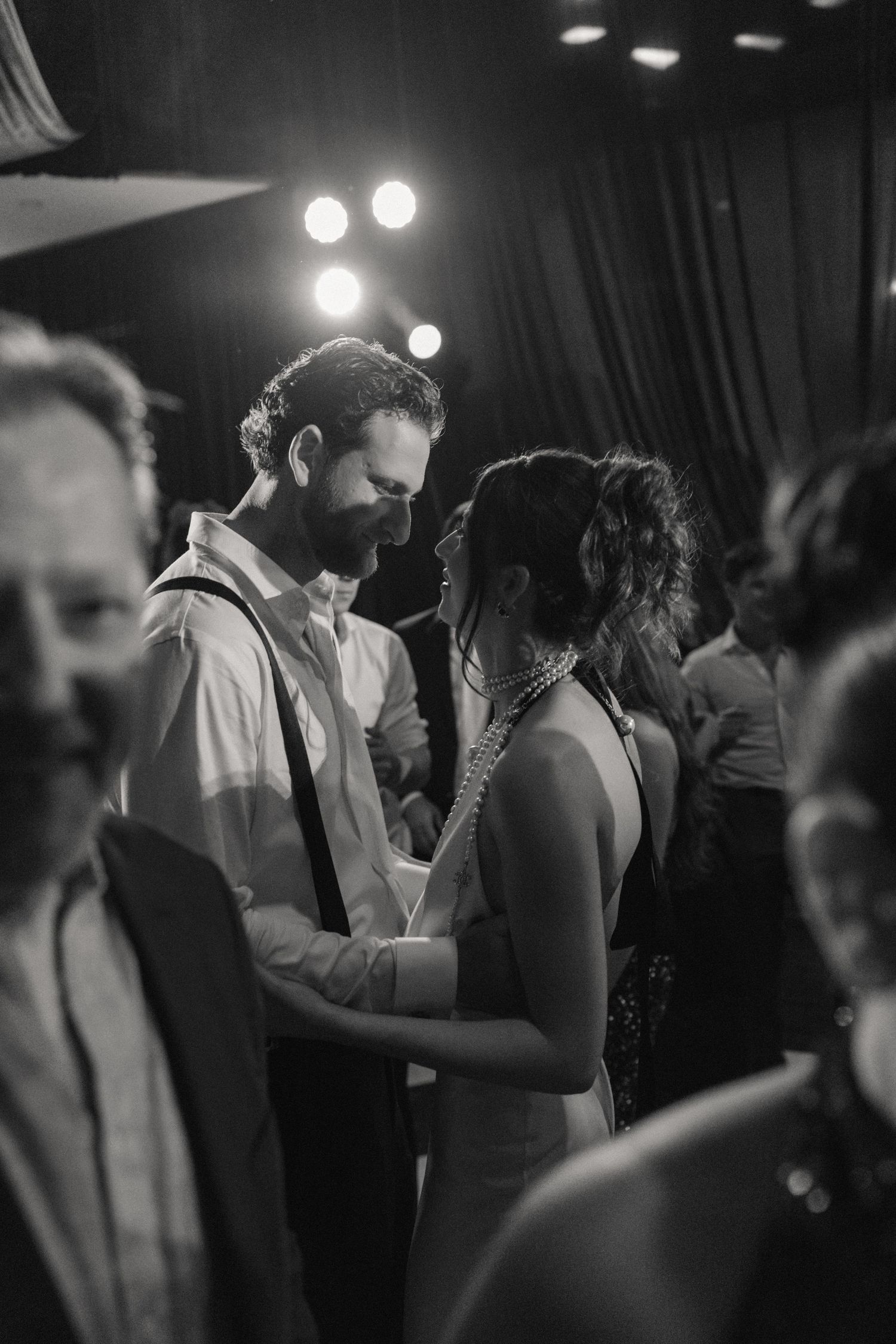 Couples slow dance together under dim lighting at an elegant wedding reception.