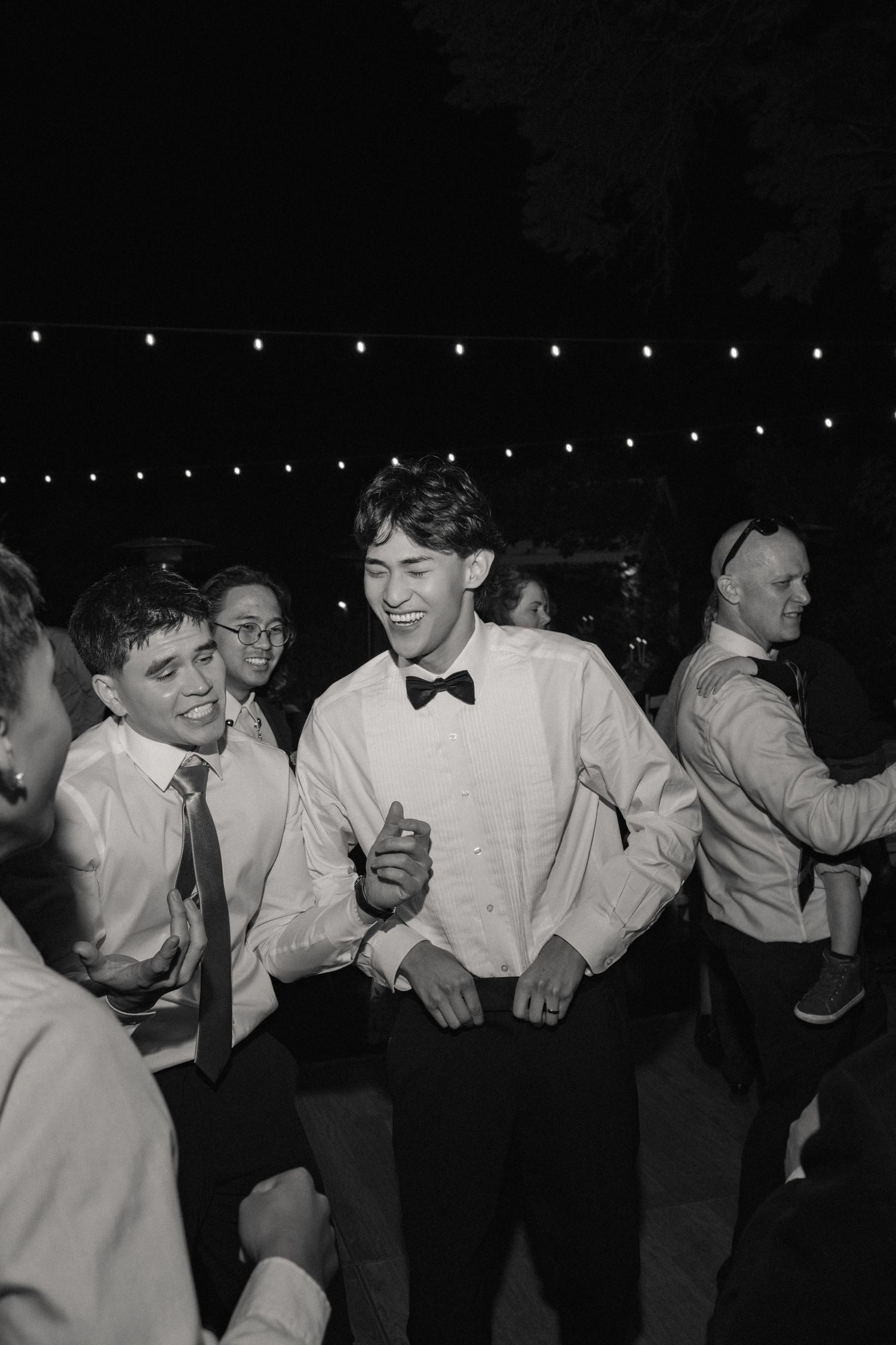Wedding party members in formal attire dance and celebrate in a line during an evening reception.