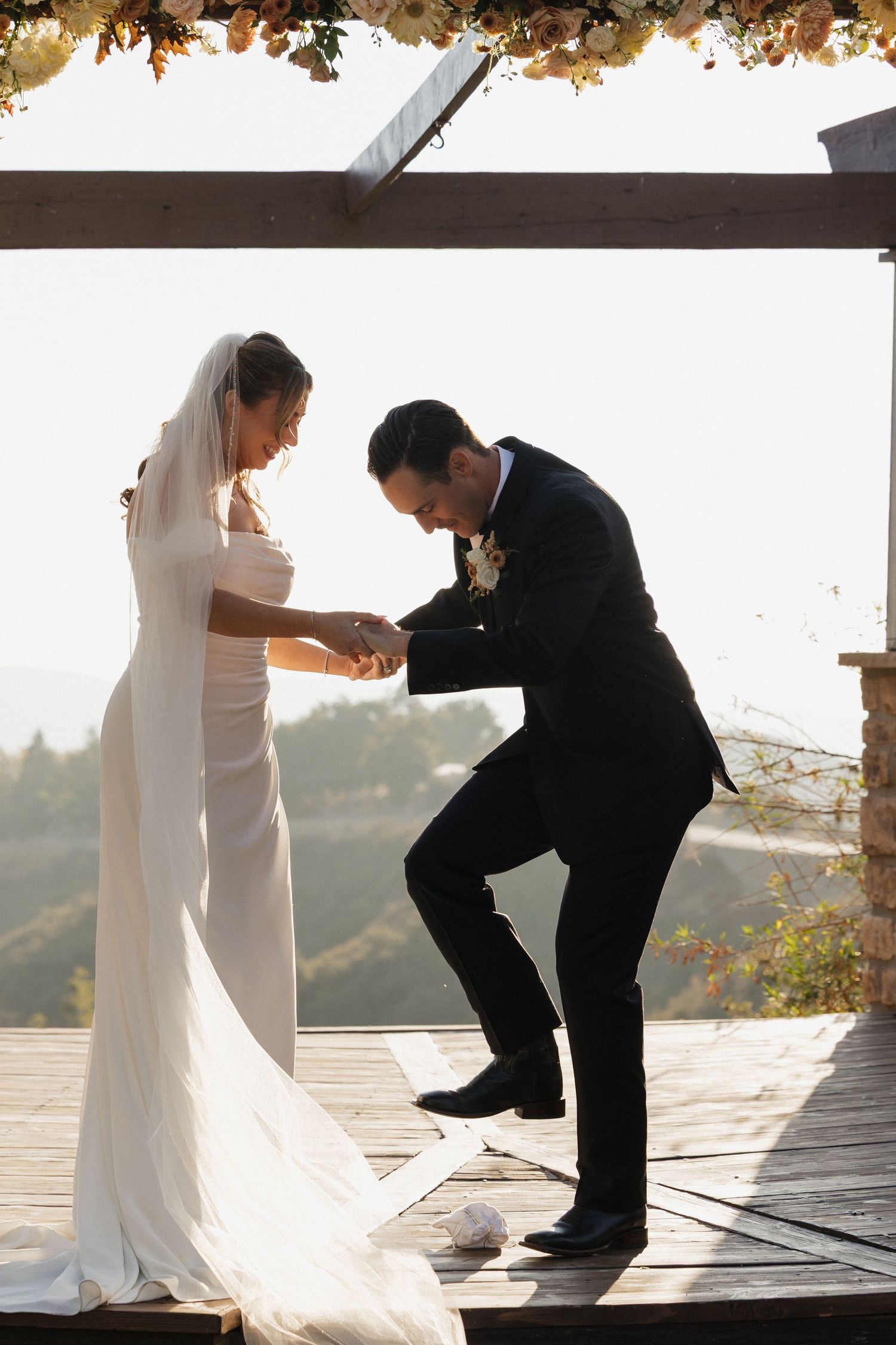 A couple shares a tender moment during their first look on a deck with autumn foliage overhead.